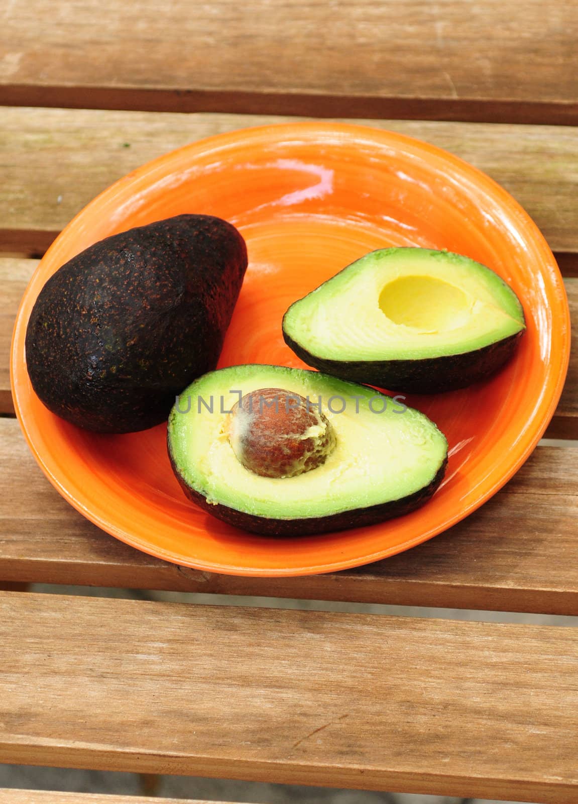 One whole and one sliced avocado on an orange plate with wood background