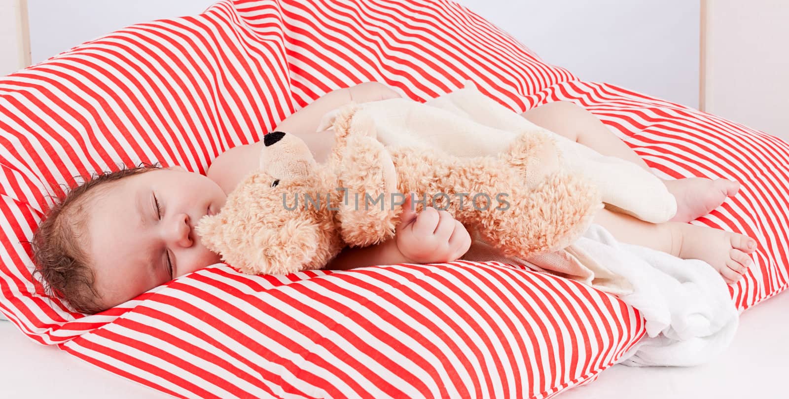 sleeping cute little baby on red and white stripes pillow with teddy bear