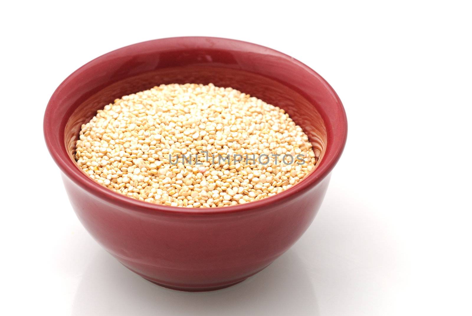 Raw whole grain quinoa in a red bowl isolated