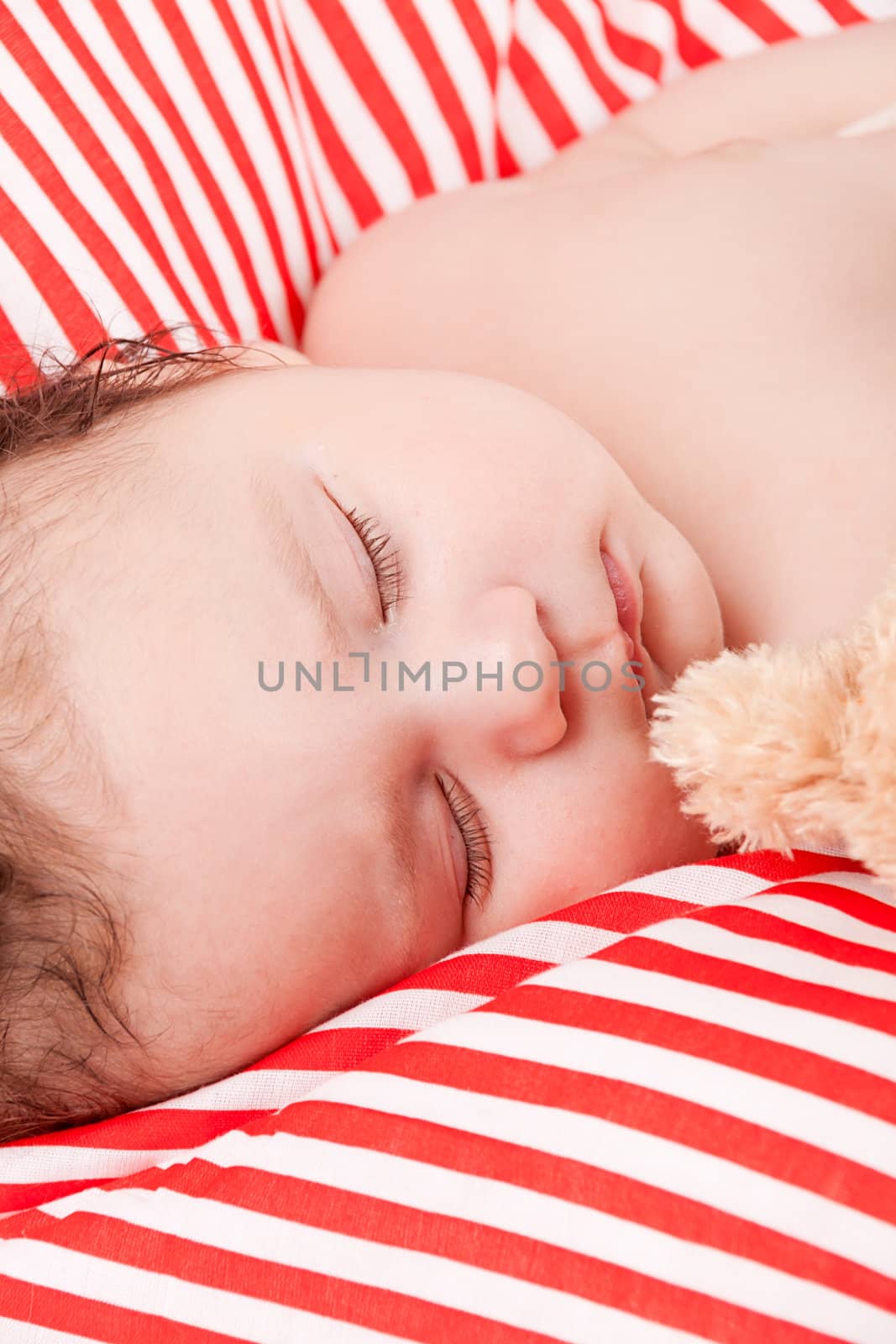 sleeping cute little baby on red and white stripes pillow with teddy bear