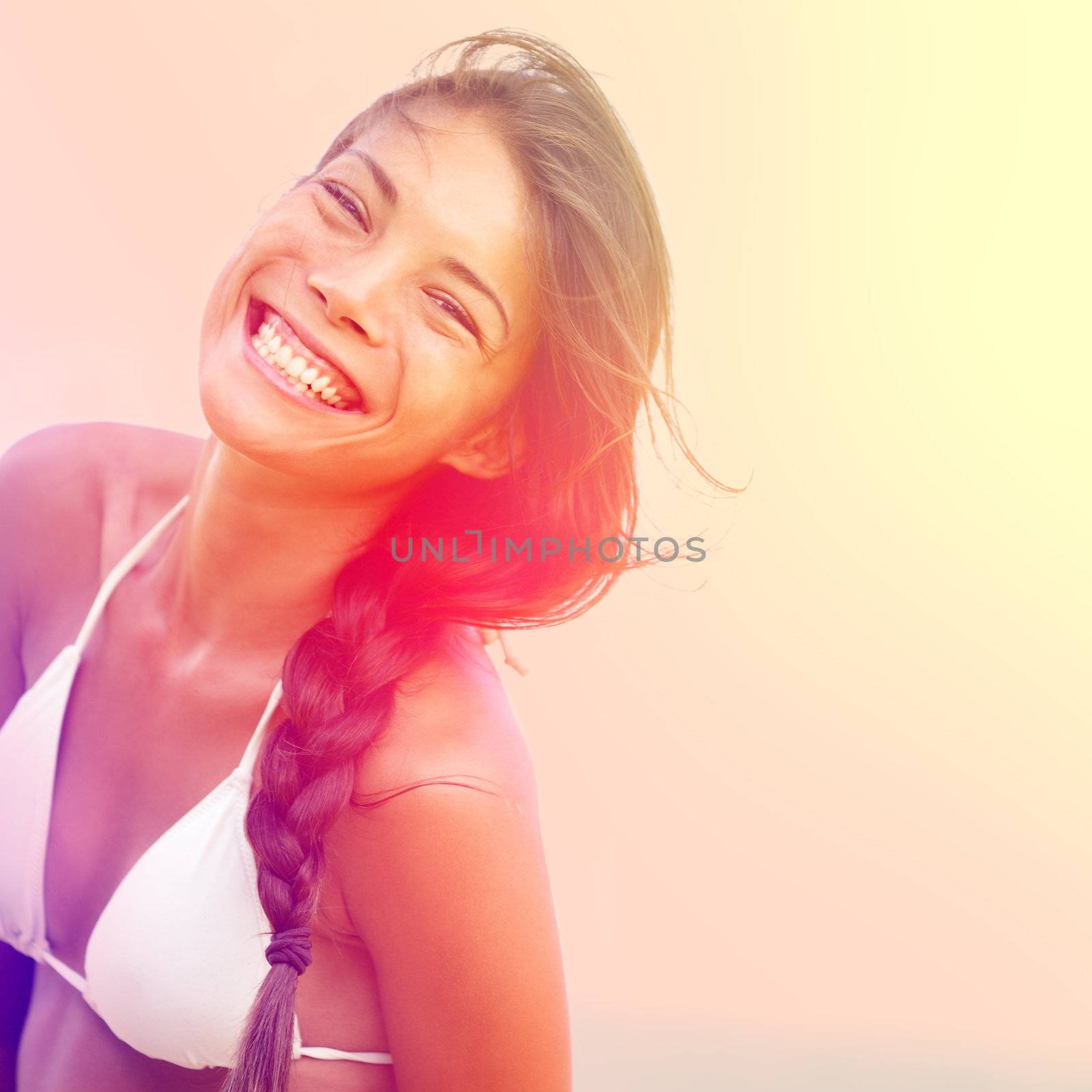 Happy sunshine woman. Girl smiling joyful, friendly and charming looking at camera on warm sunny summer day under the hot sun on beach. Beautiful multicultural Asian / Caucasian female bikini model.