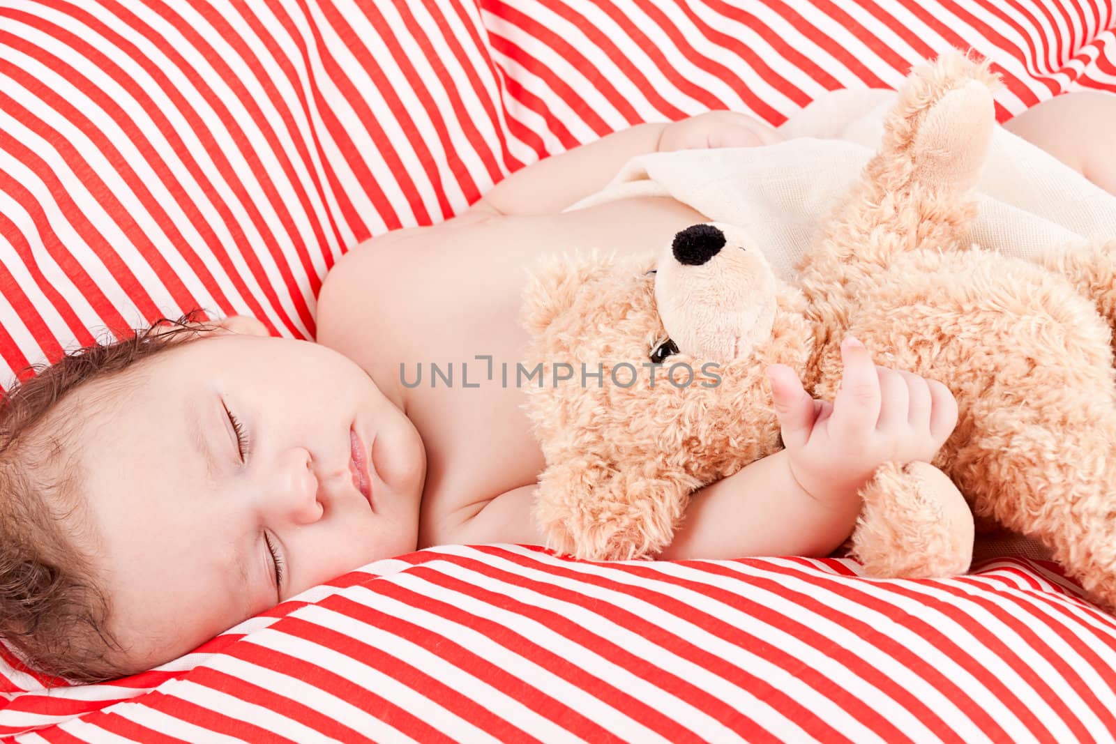 sleeping cute little baby on red and white stripes pillow with teddy bear