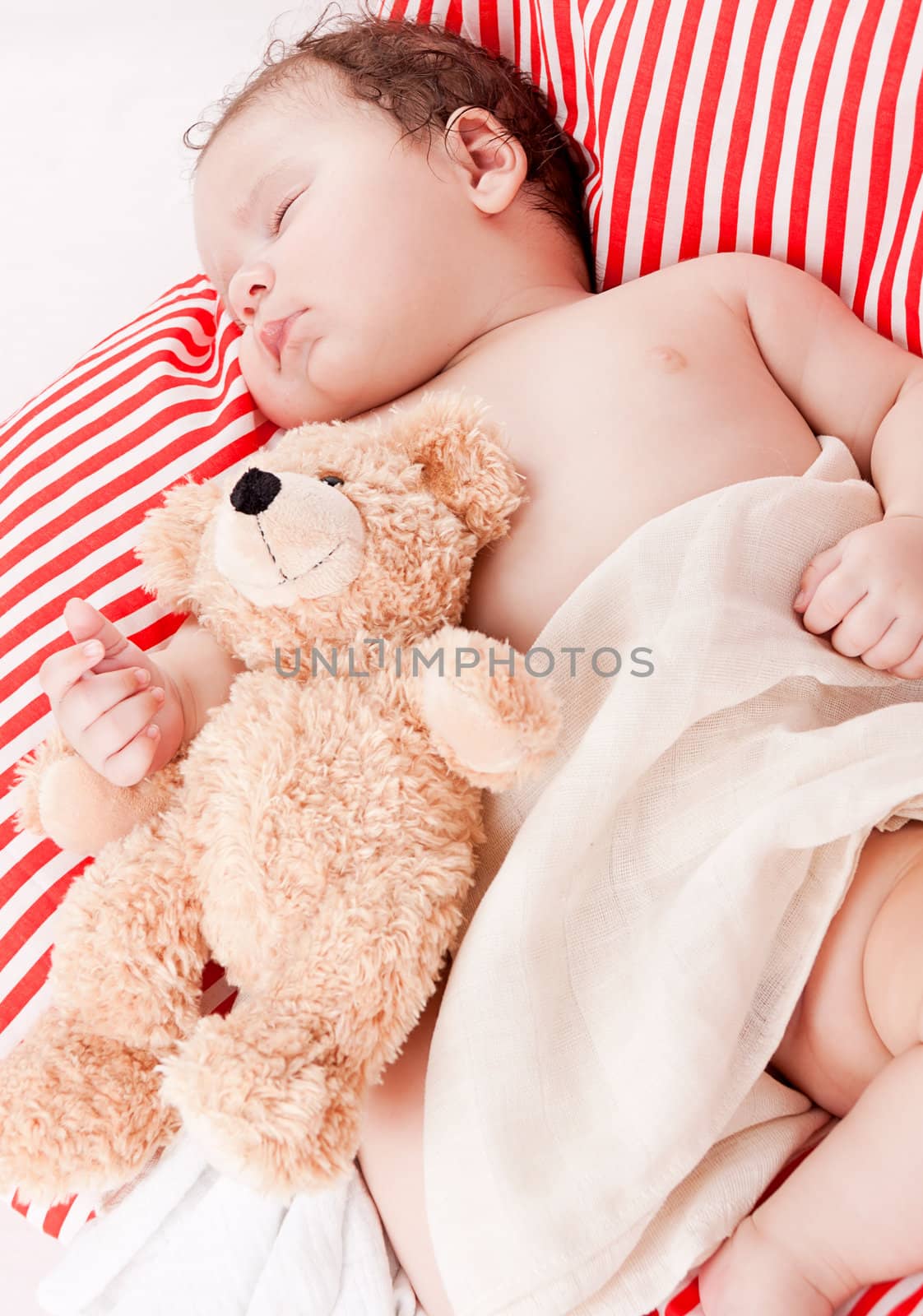 sleeping cute little baby on red and white stripes pillow with teddy bear