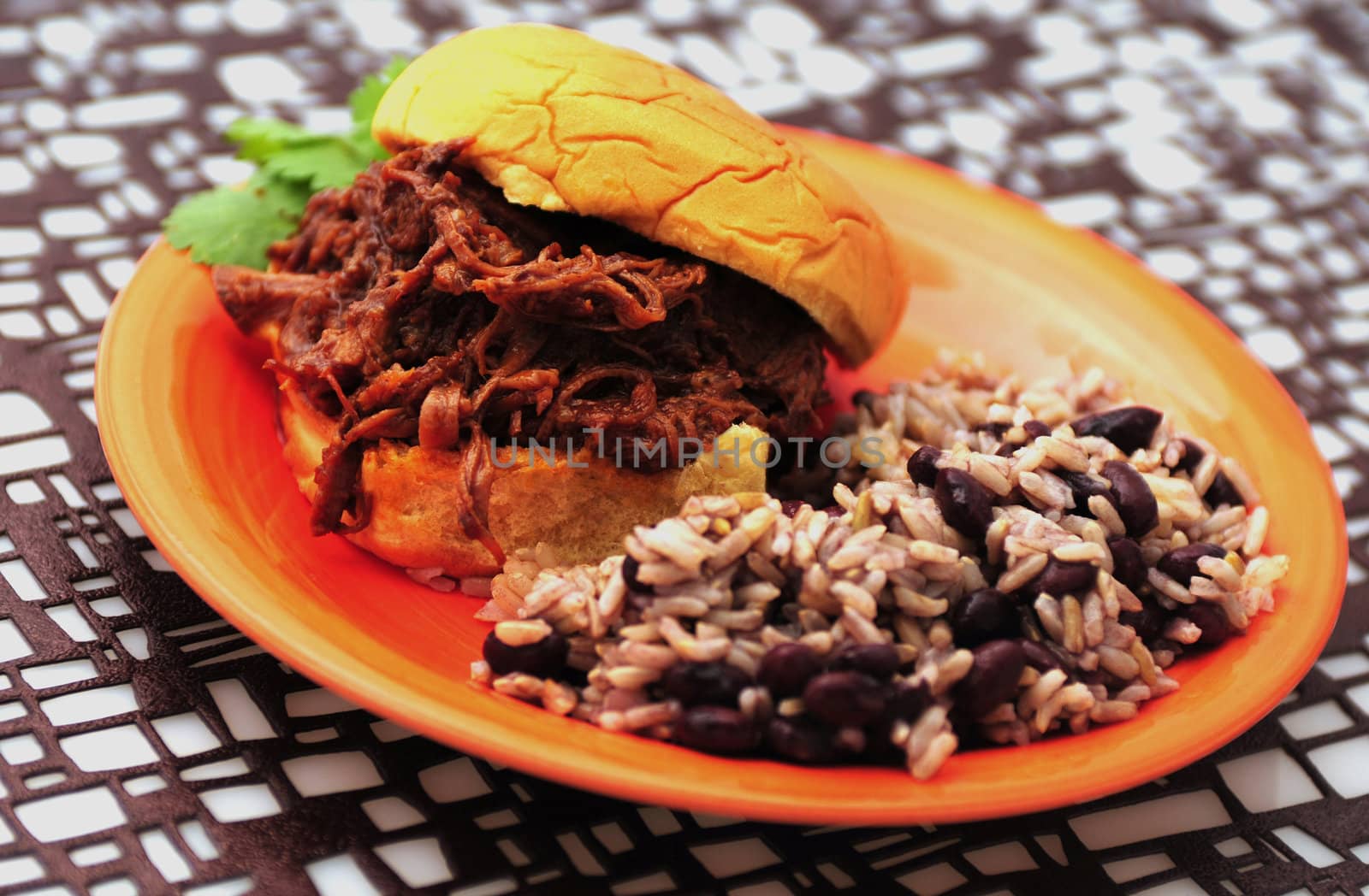 A shredded beef sandwich with beans and rice on a a geometric place mat