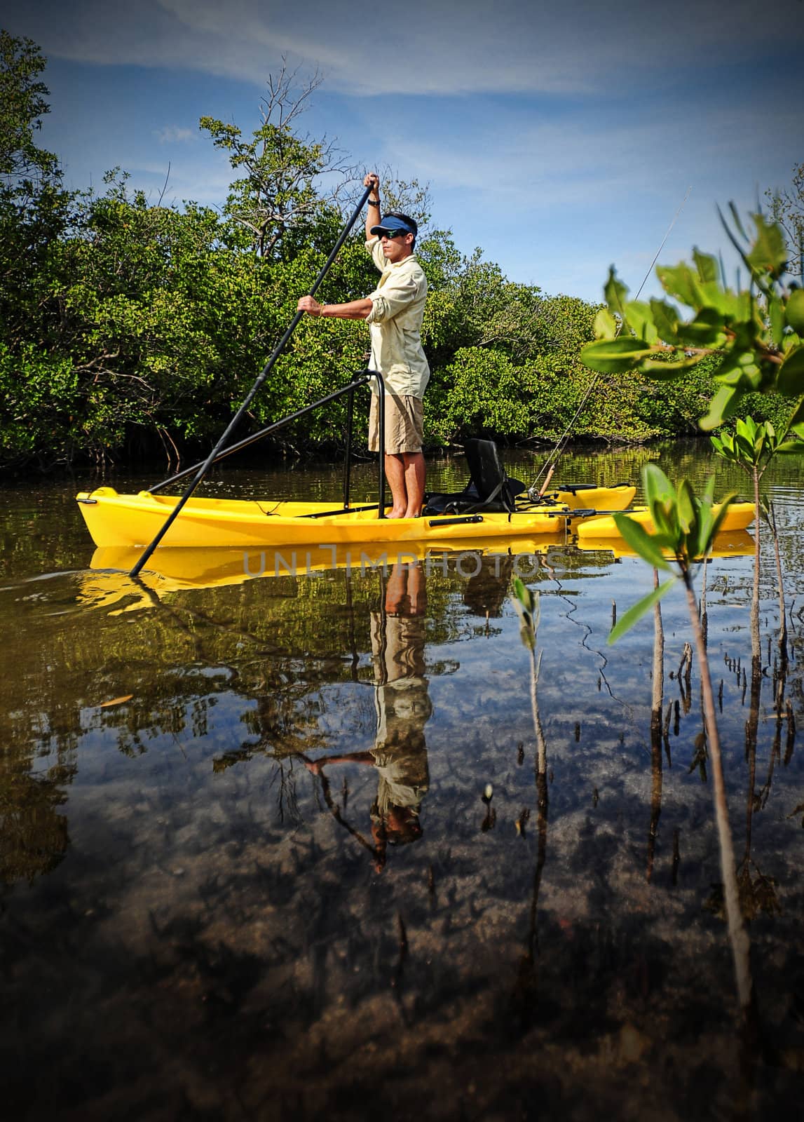 Man paddling down river on a yellow kayak with fishing pole