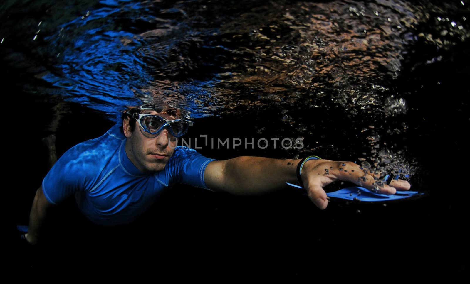 Man swimming underwater in pool with resistance swim paddles for exercise