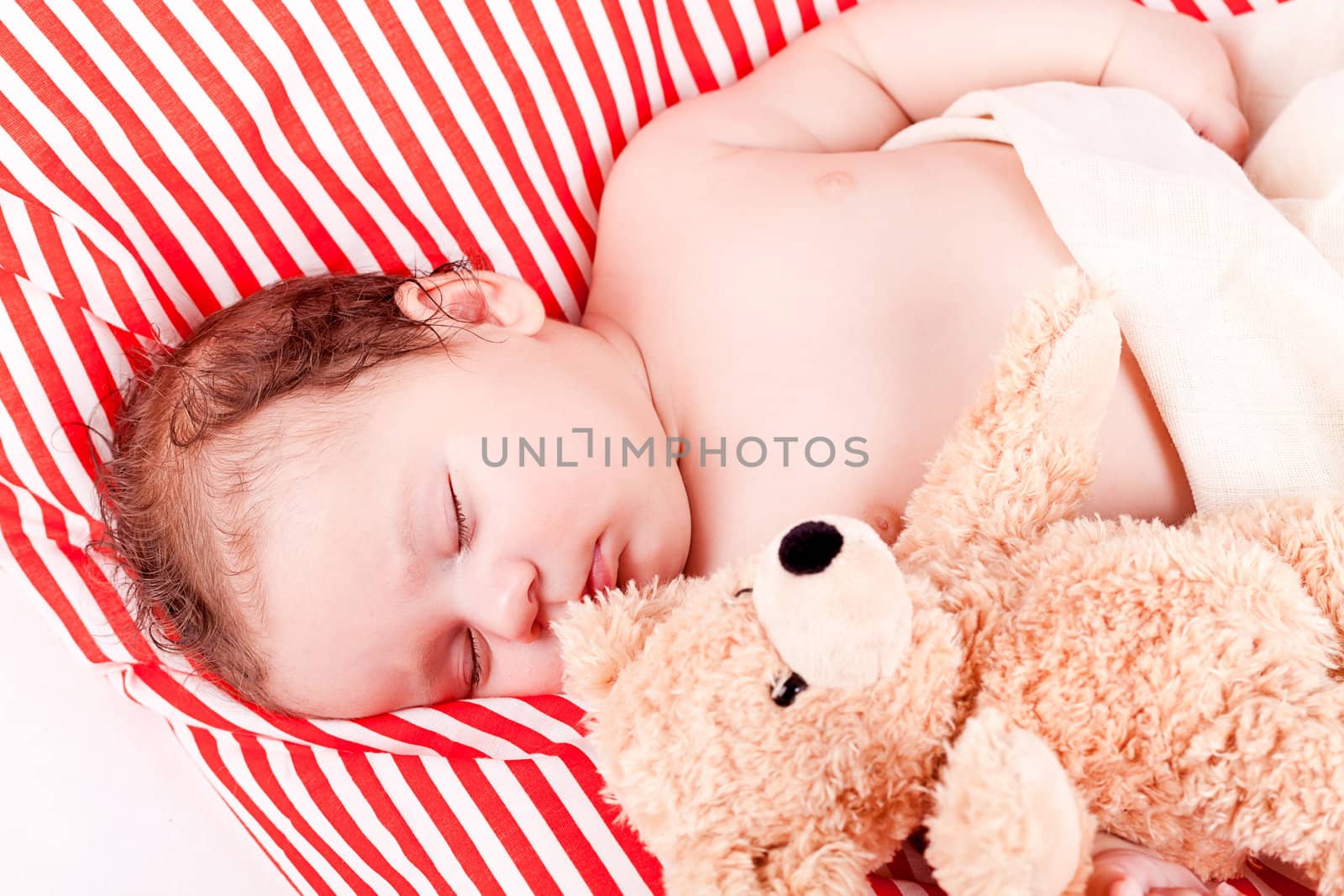 sleeping cute little baby on red and white stripes pillow with teddy bear