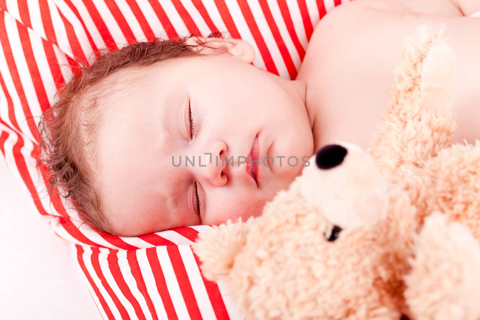 sleeping cute little baby on red and white stripes pillow with teddy bear