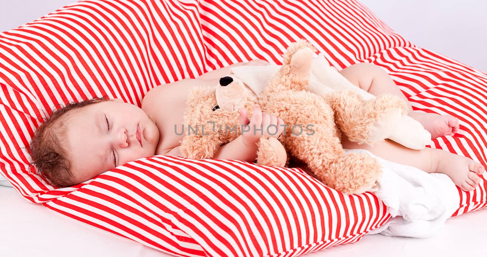 sleeping cute little baby on red and white stripes pillow with teddy bear