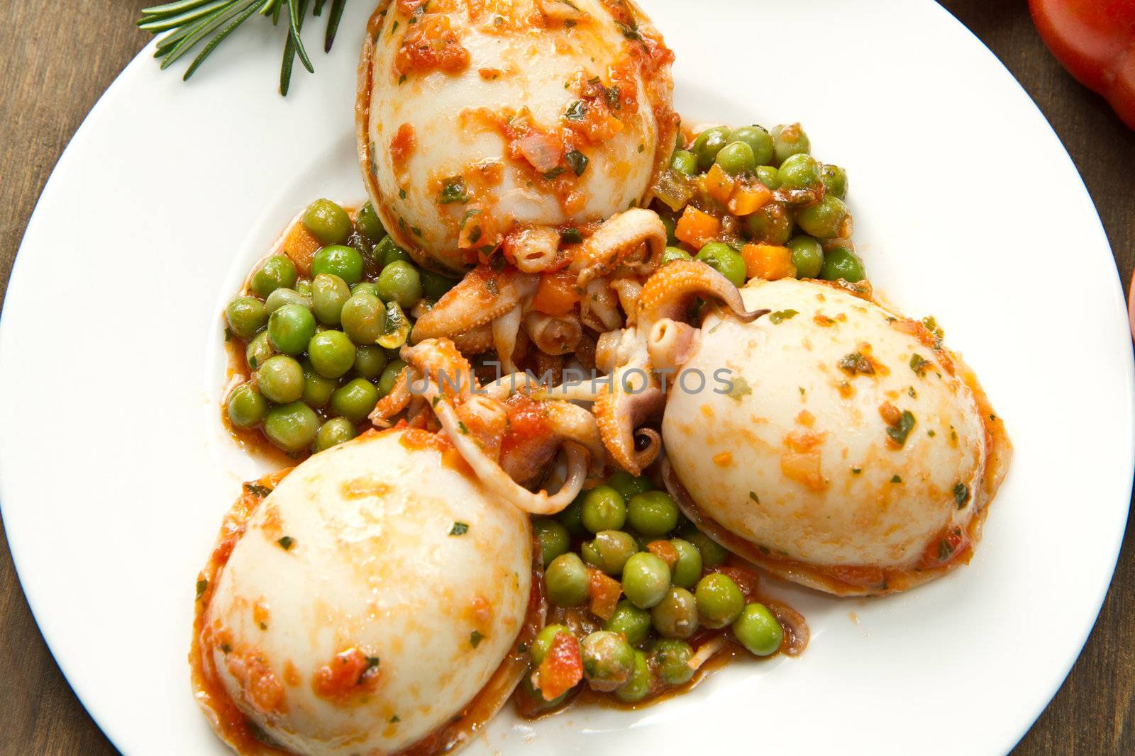 a white bowl with cuttlefish with peas and fresh tomatoes, lemon and oil