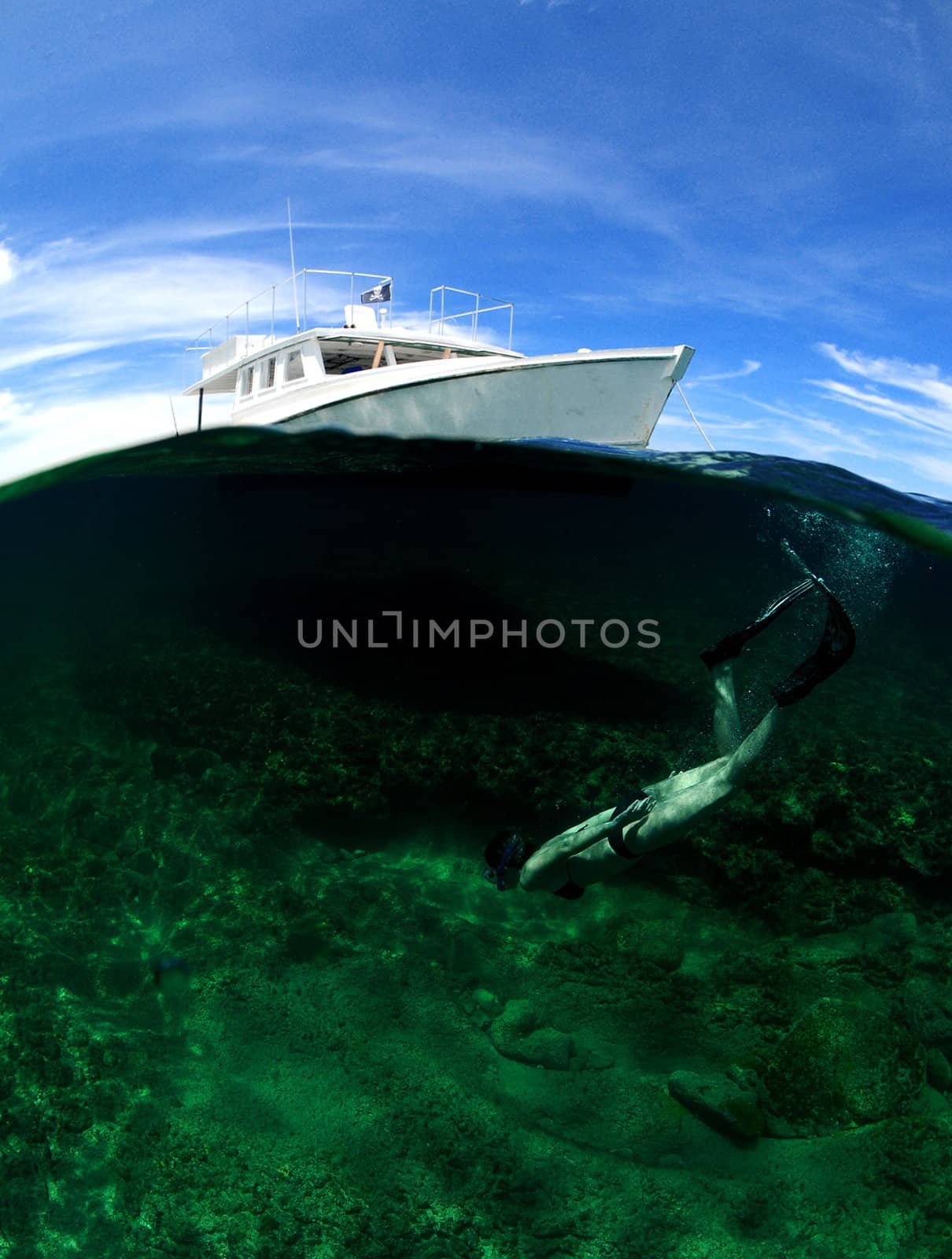 Underwater view of woman snorkeling with an above ground view of a white boat against a blue sky