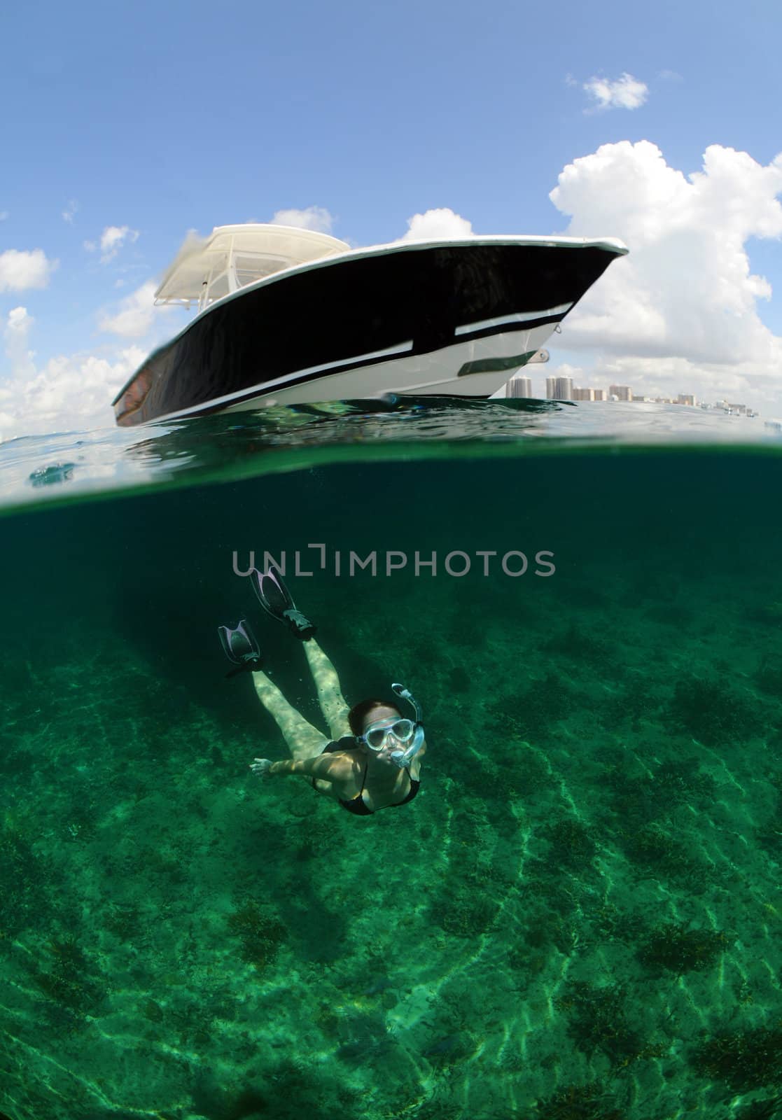 Pretty woman snorkeling underwater with boat and blue sky in background