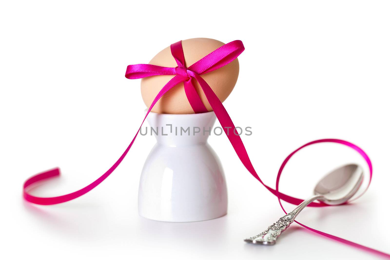 Easter egg with pink ribbon on white background. Composition with silver teaspoon and egg hand painted a beige paint