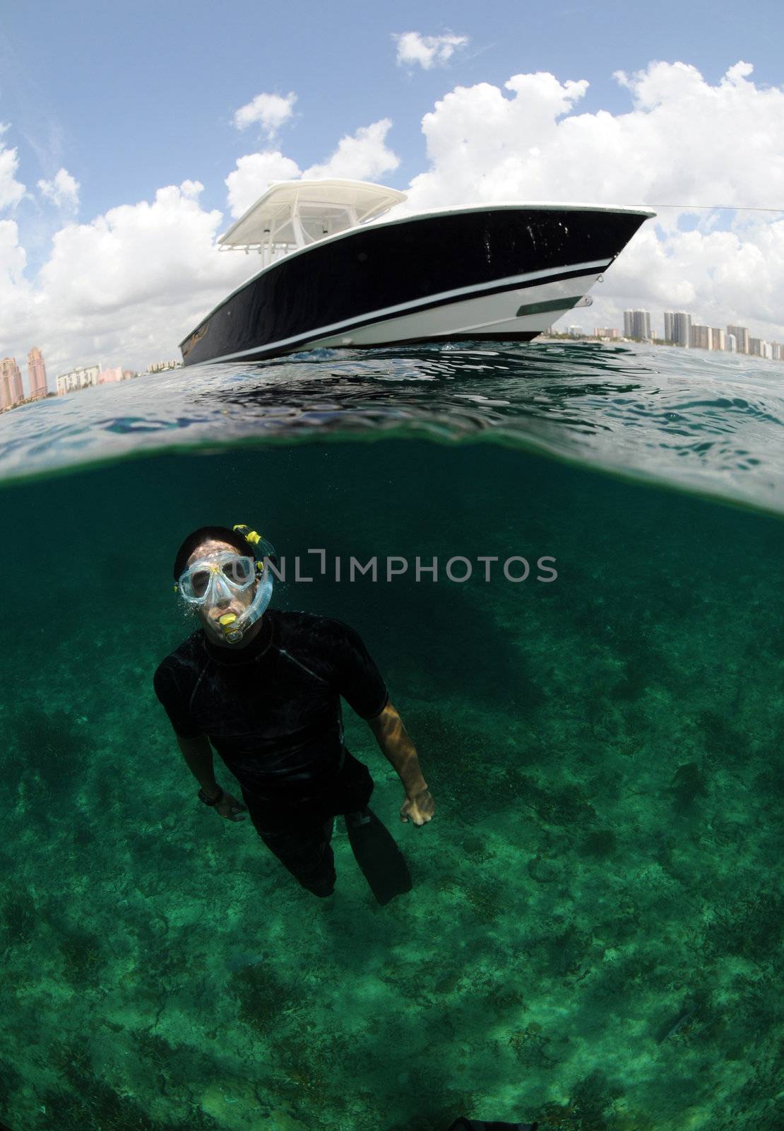 Young man snorkeling with boat and city in background