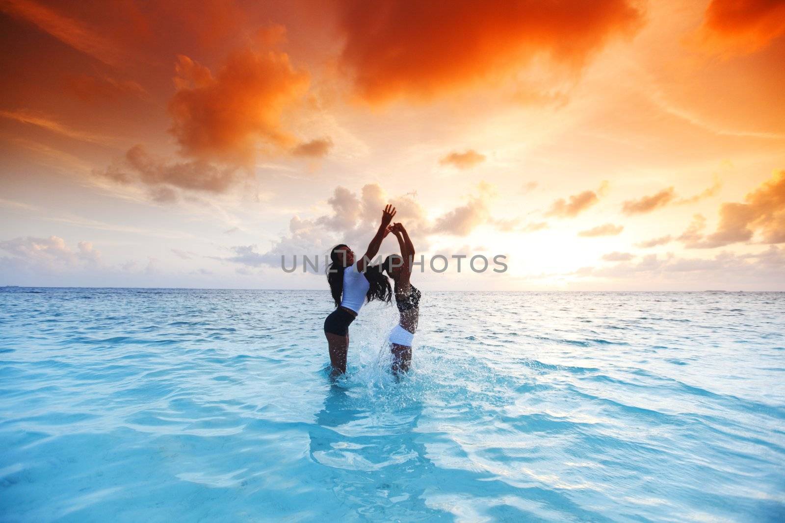 Two happy wimen playing in water on sunset