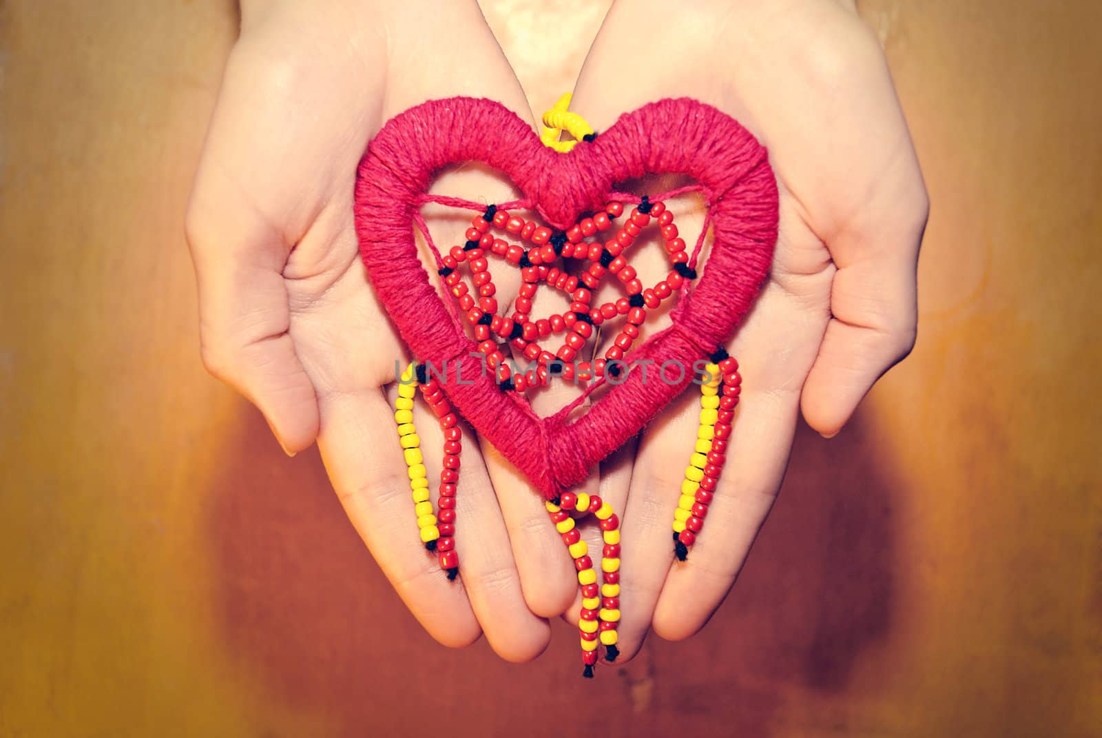 Red heart of colored beads in female hands.