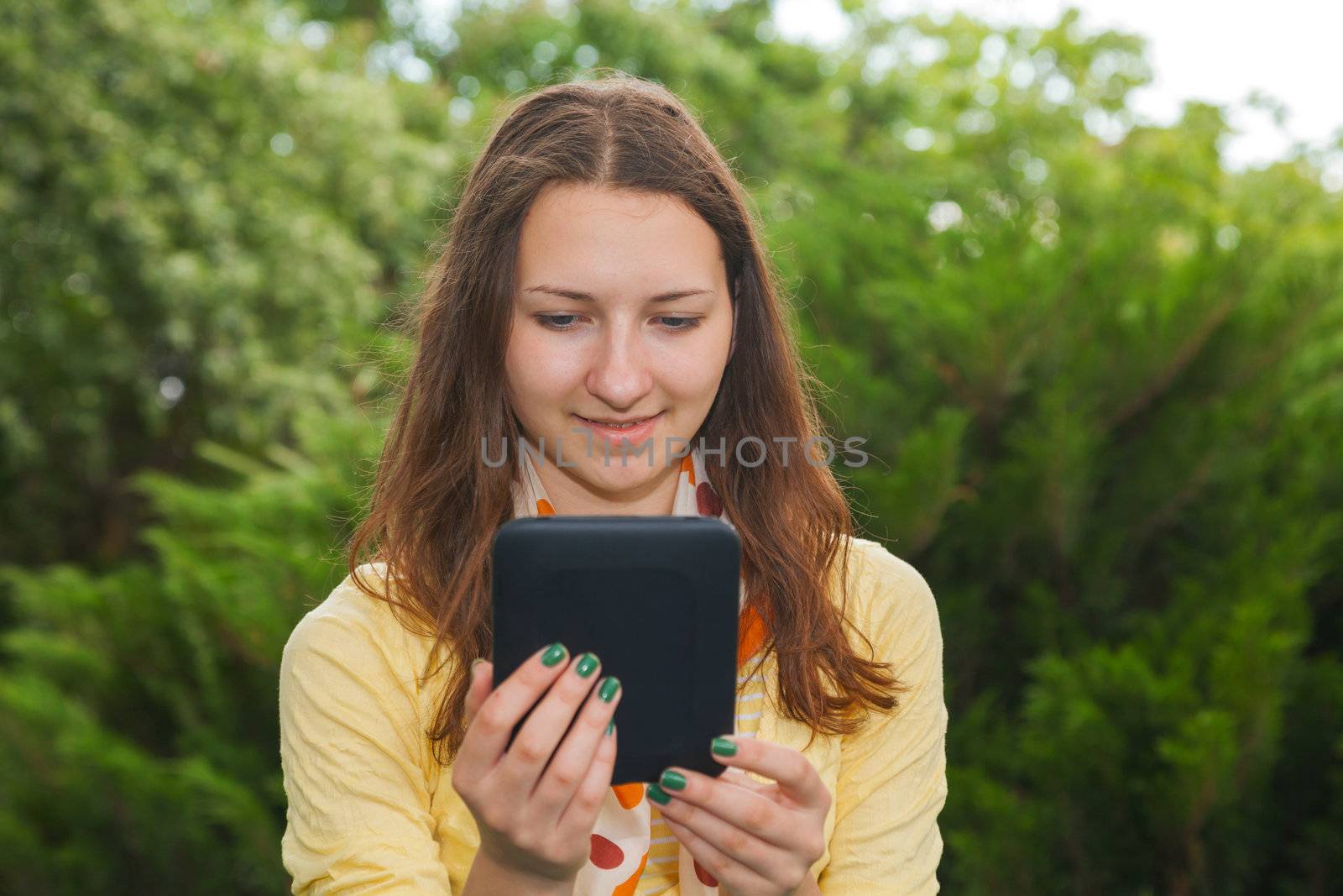 Teen girl reading electronic book outdoors