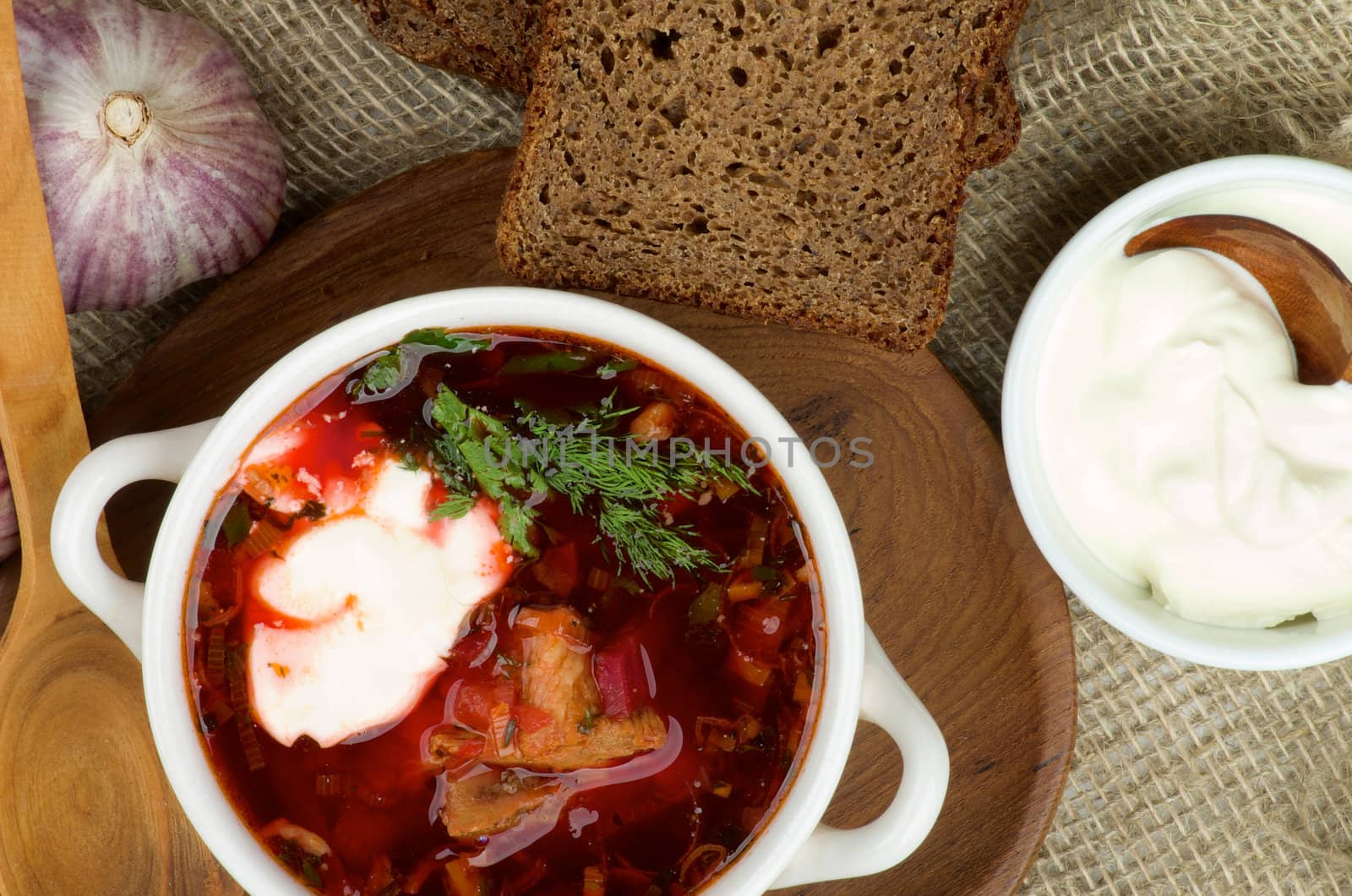 Ukrainian National Traditional Soup with Beet, Vegetables and Meat. Top View of Borscht on Wooden Plate and Brown Bread, Garlic, Bowl of Sour Cream on Sackcloth backrgound