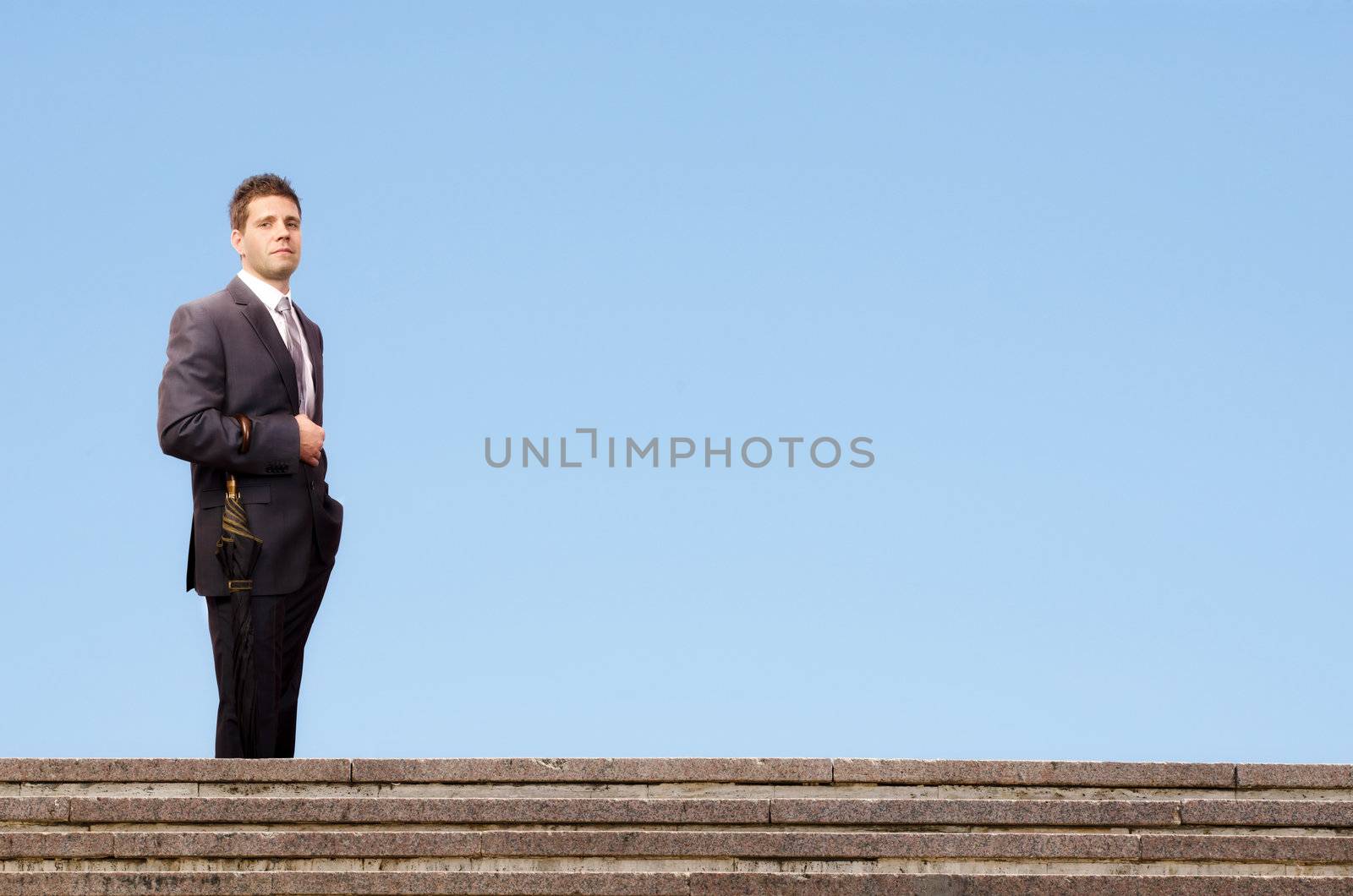 Successful businessman standing on stairs against a blue sky background