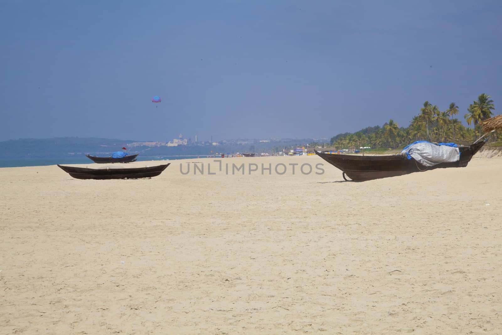 Landscape of secluded beach with white sand, blue sky, sea, surf, para gliders and fishing boats for a backdrop. Generic tropical shot location, Goa India