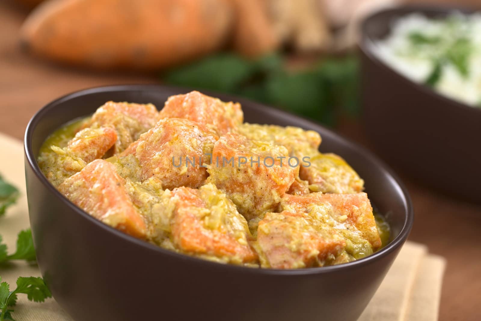 Bowl of vegetarian sweet potato and coconut curry with cooked rice and ingredients in the back (Selective Focus, Focus one third into the curry dish)