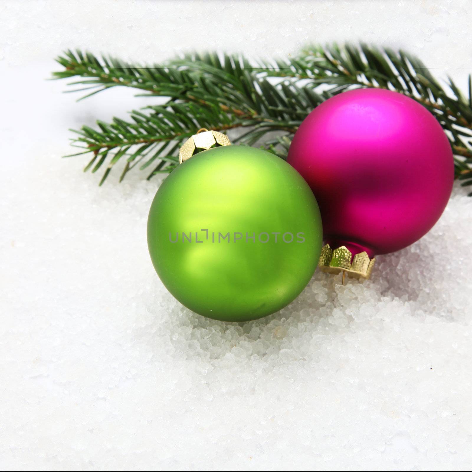 Two colorful Christmas baubles on and pine tree branches on snow