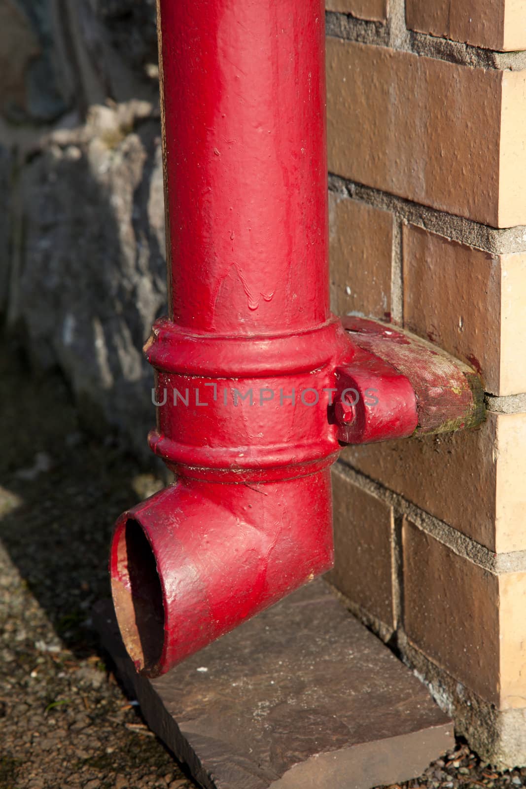 The foot of a downpipe with joint and end piece painted red and fixed to a brick wall.