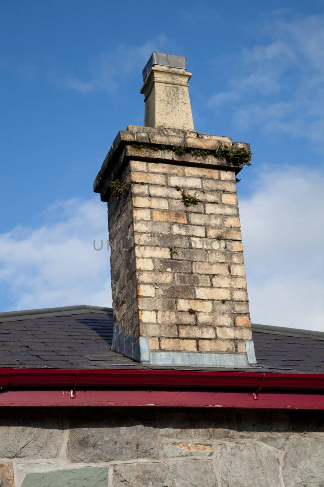 A yellow brick chimney with pot and flashings on a slate roof.