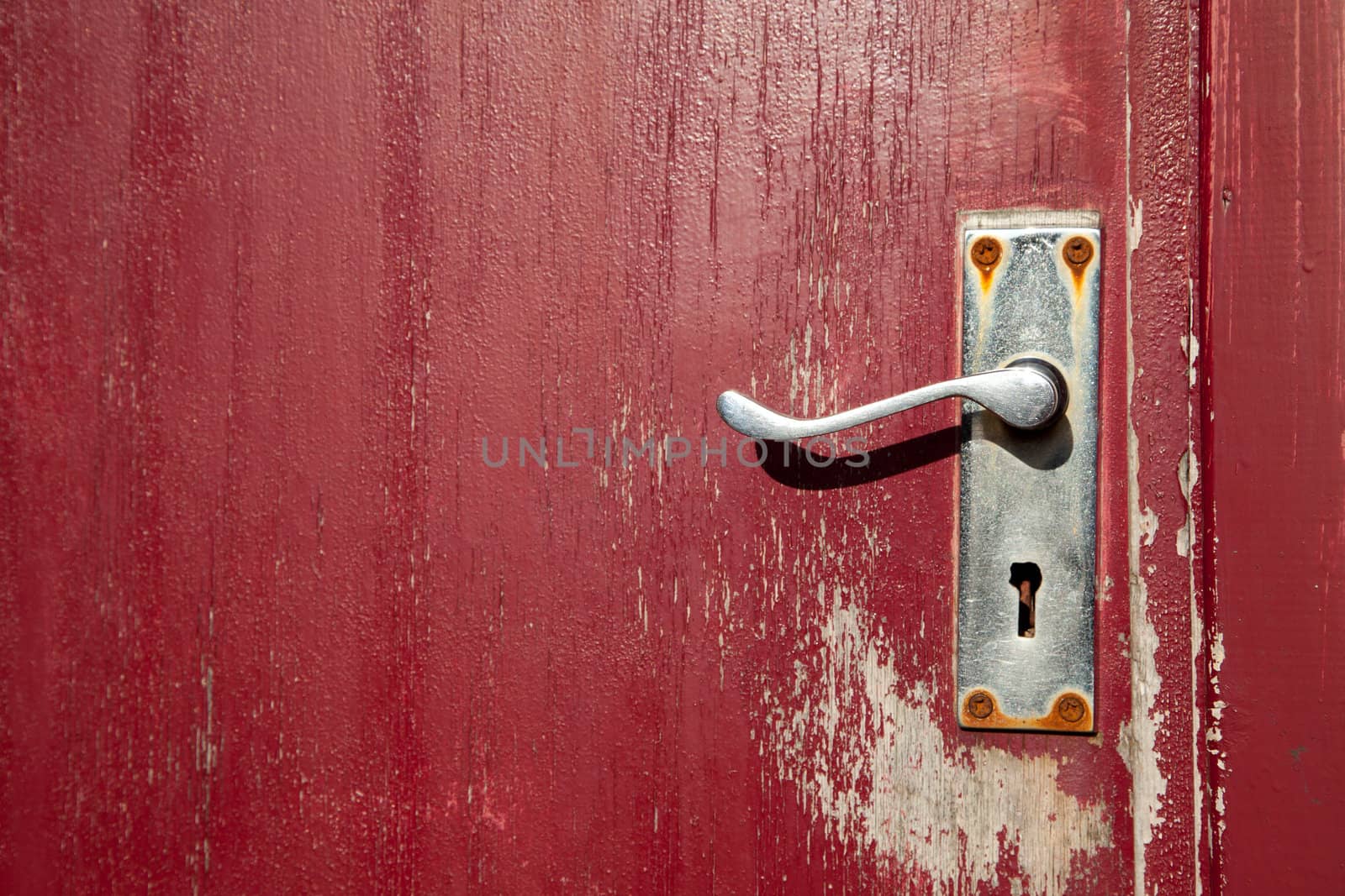 A red painted wooden door with an old door handle with keyhole.