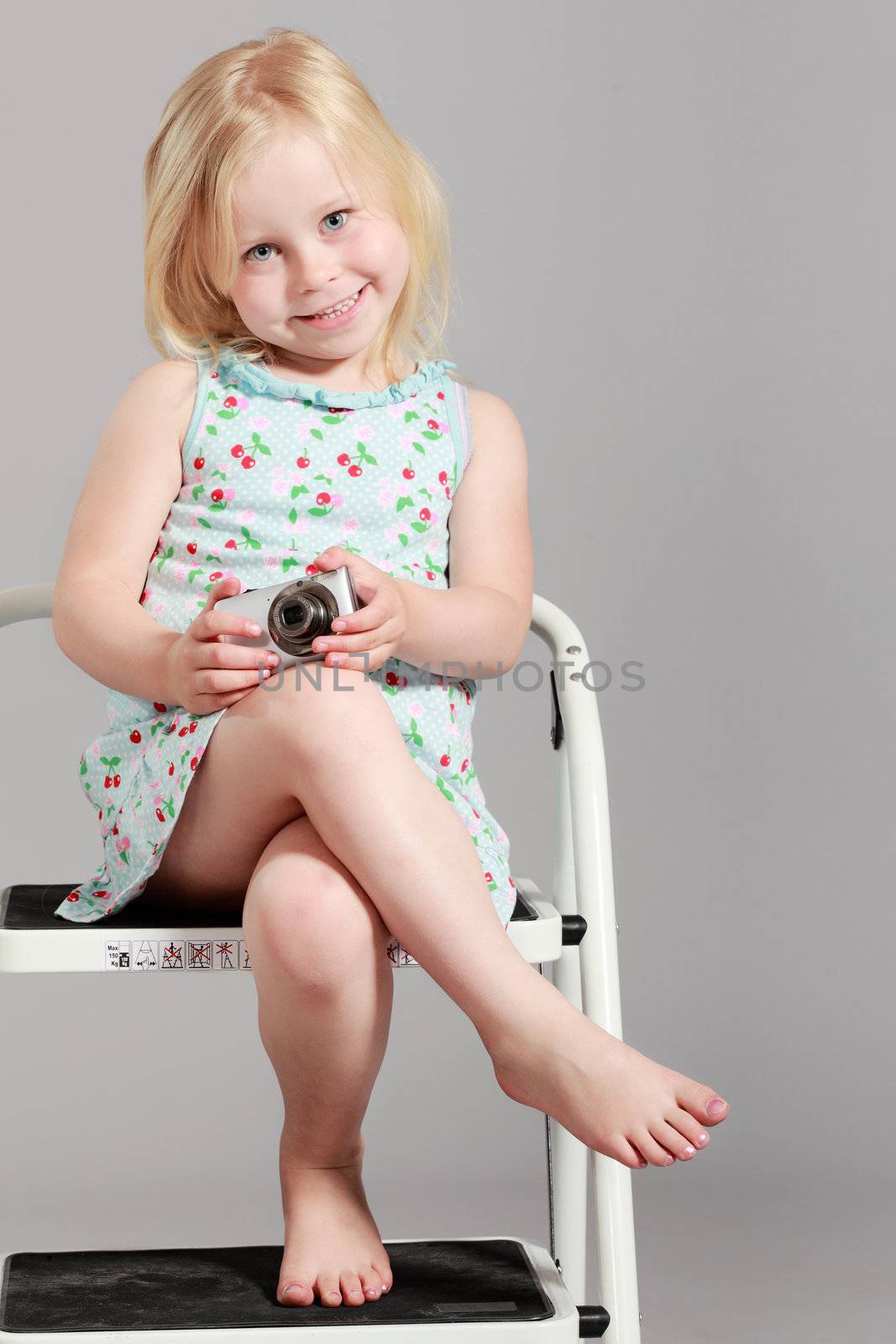 cute little girl sitting on a ladder against gray background