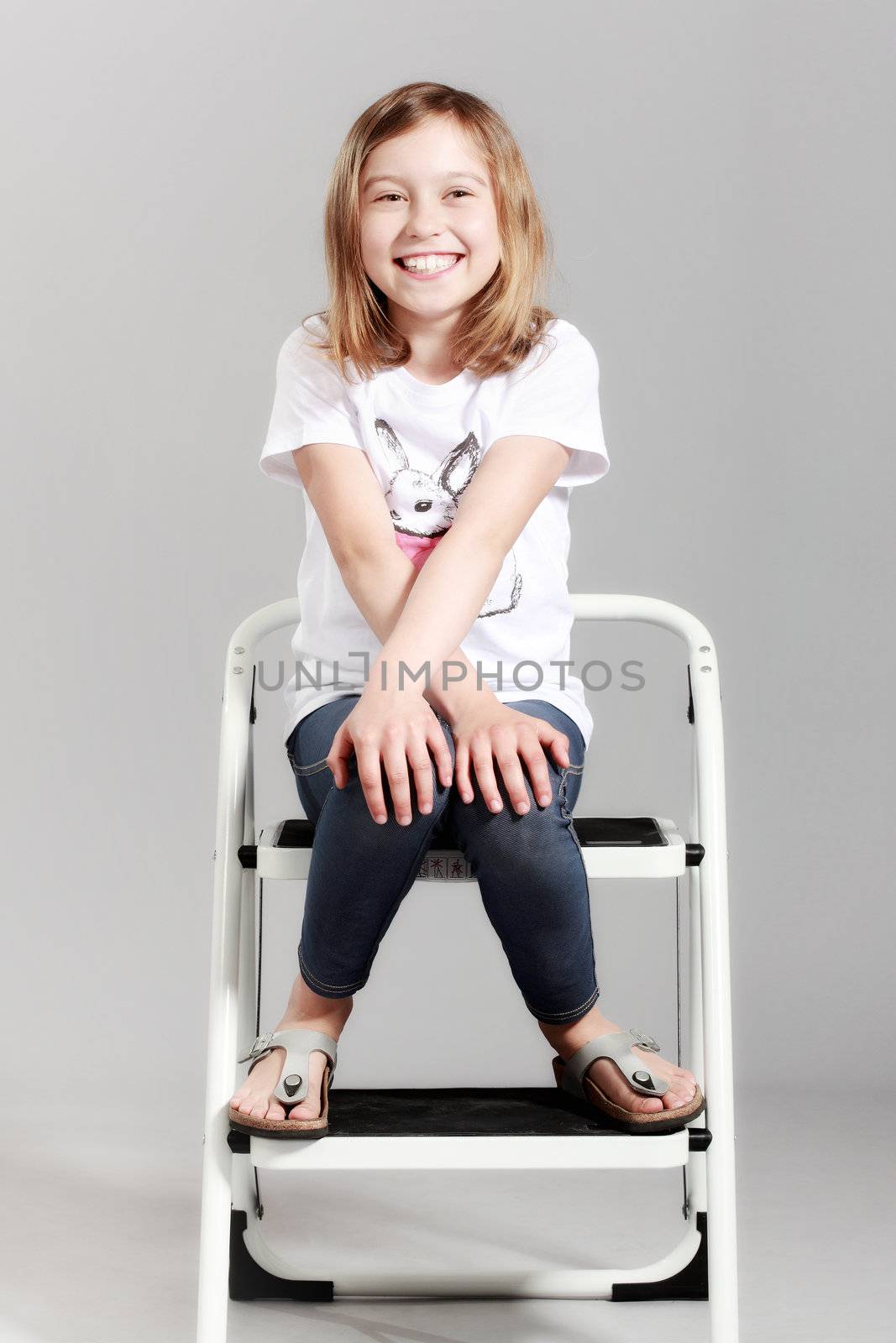 cute little girl sitting on a ladder against gray background