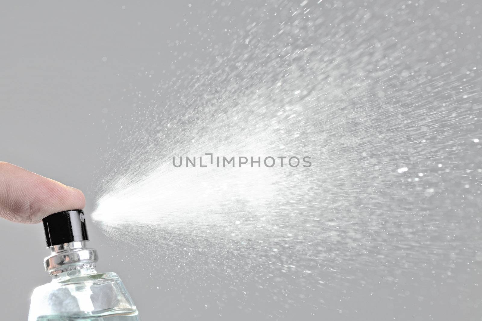 bottle spraying perfume against gray background