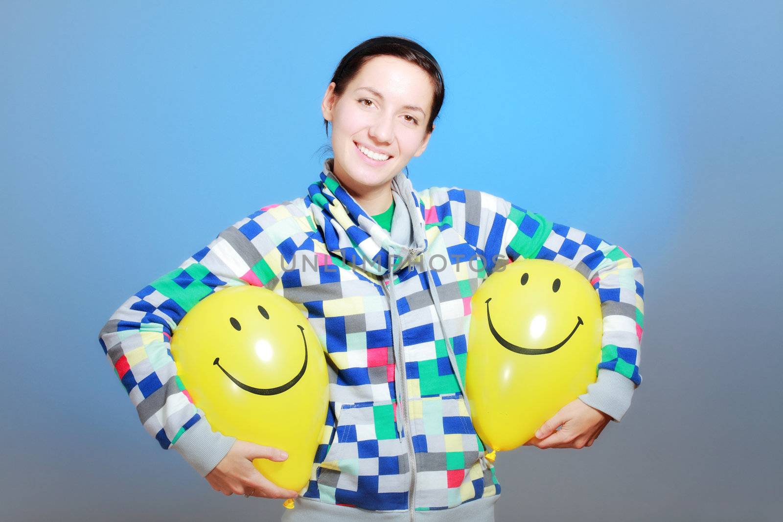 girl with two yellow smiley balloons against blue