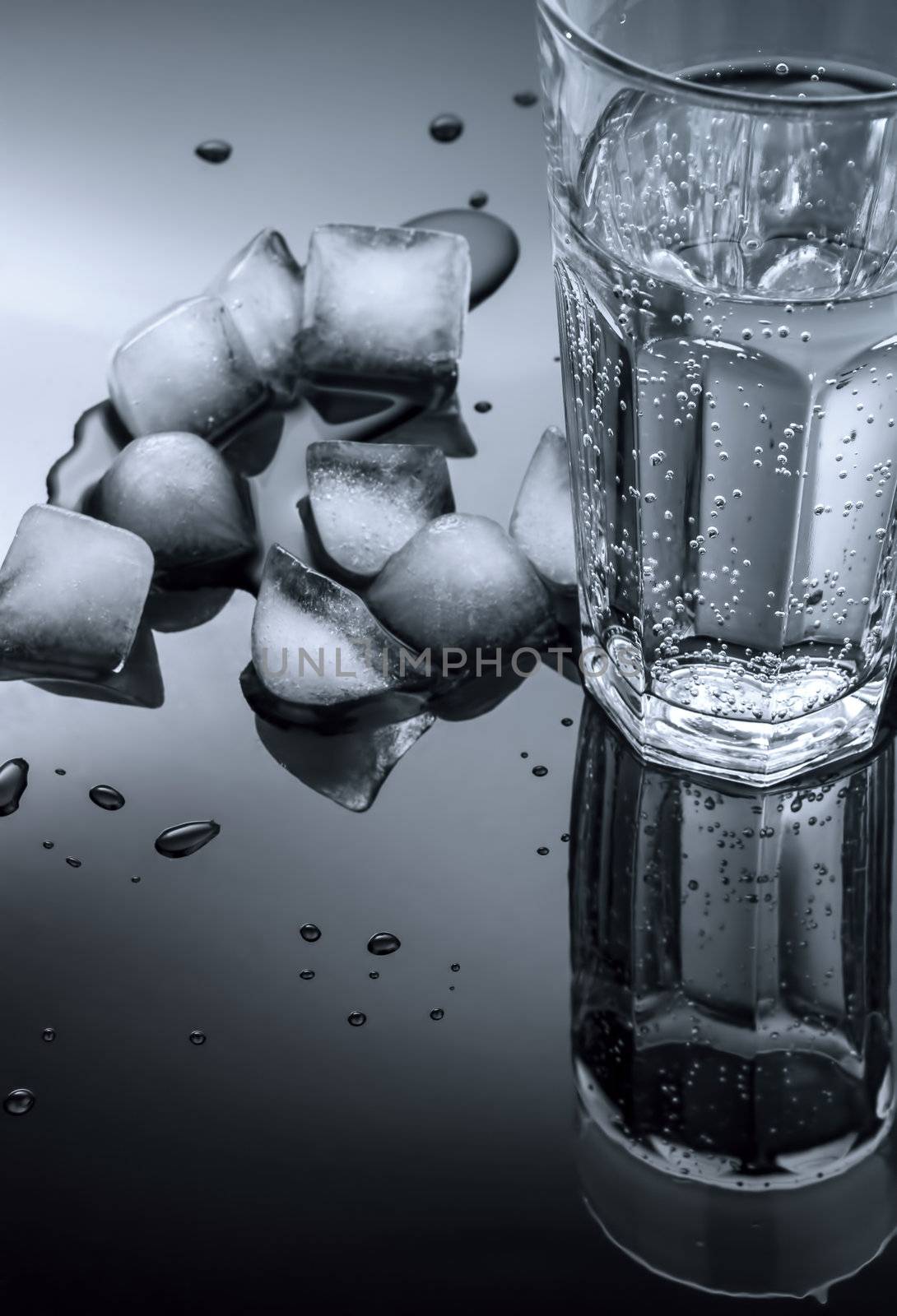 glass of water and ice cubes on a dark background of the mirror