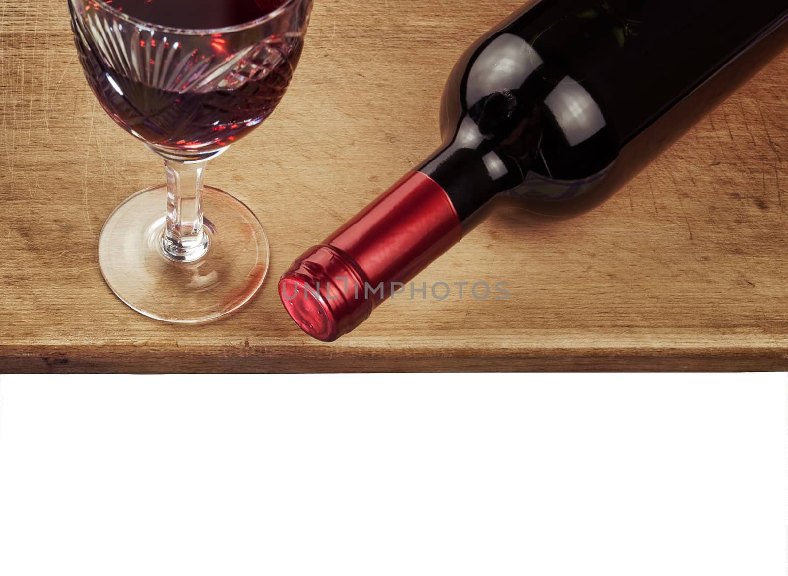 bottle of red wine and glass of wine against a wooden table on white background