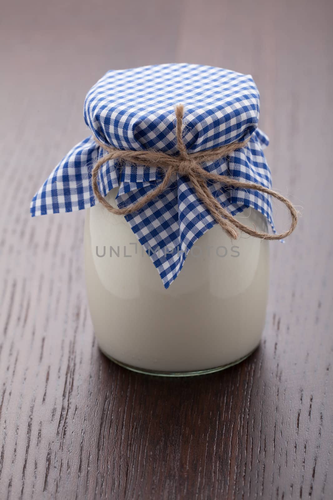 Homemade milk yogurt in glass pot served with linen napkin on wooden table