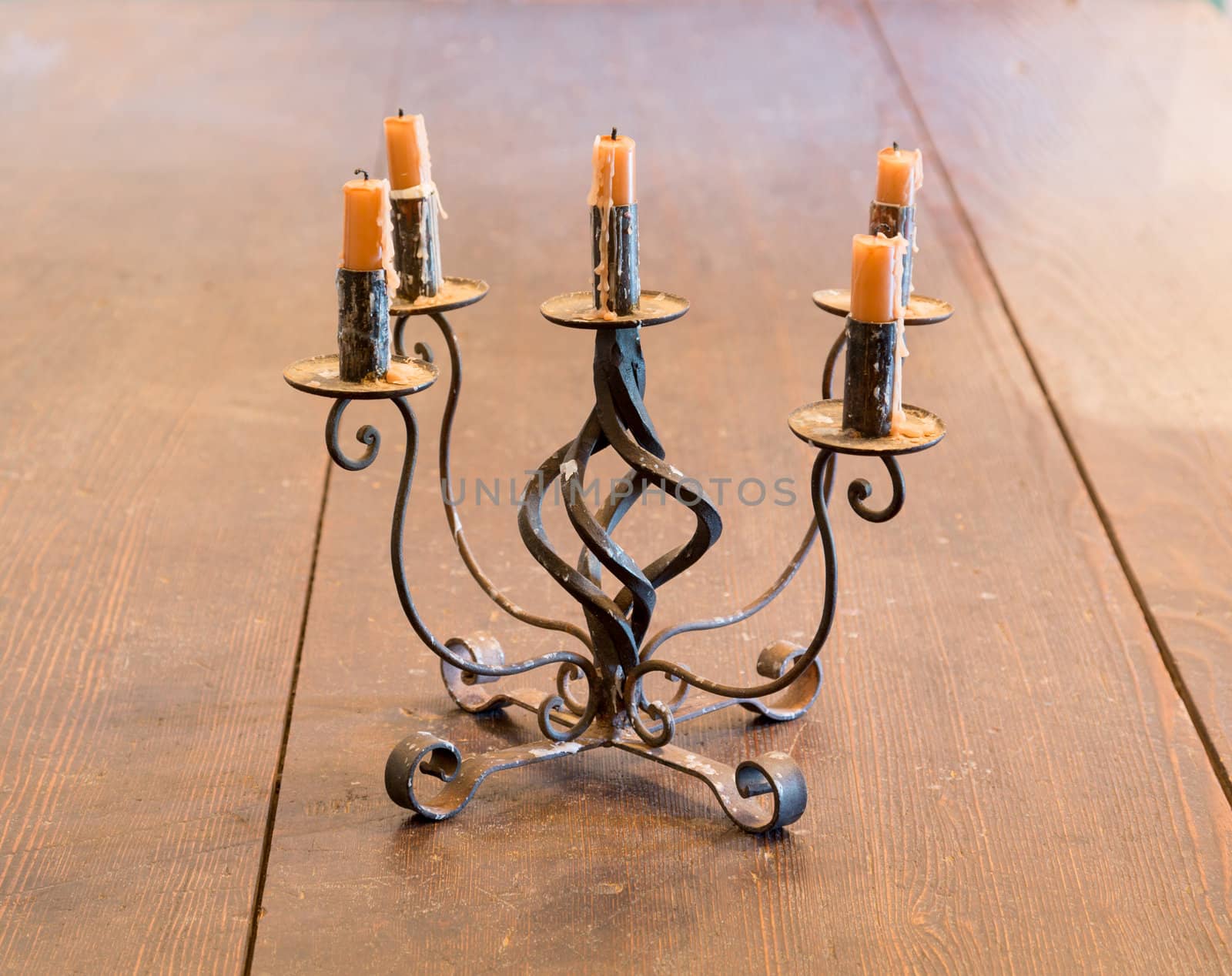 Old iron candlestick holder and candles lit by light from window on old wooden table