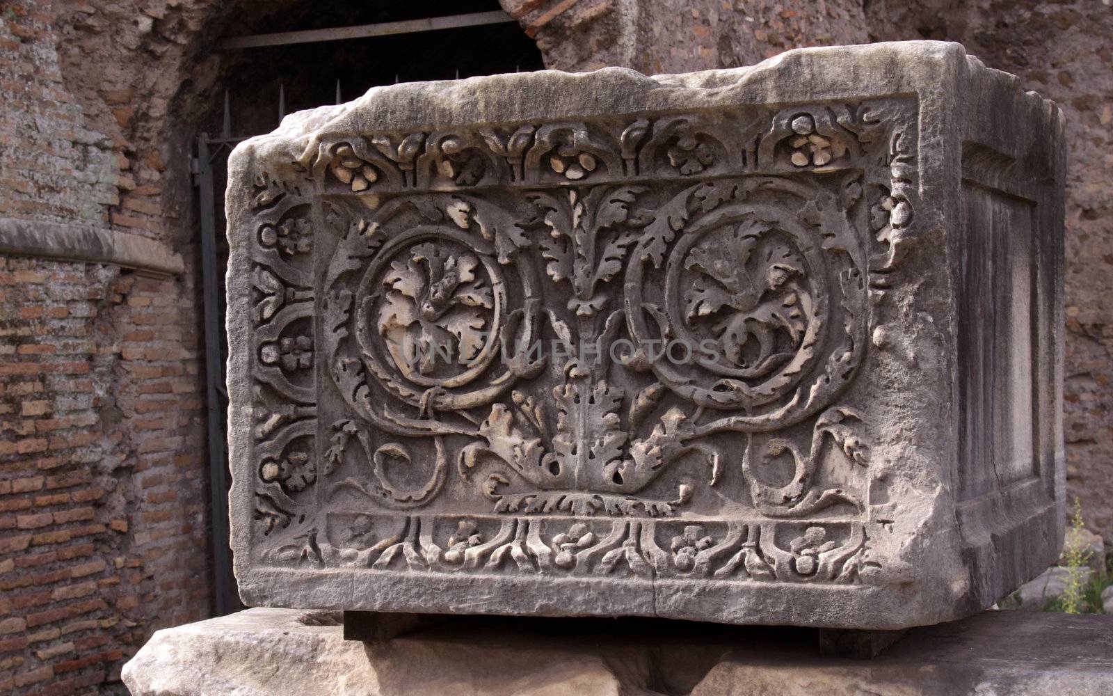 A stone block carved with a floral decoration created by the Roman Empire.  The block is located in the Roman Forum in Rome, Italy. 