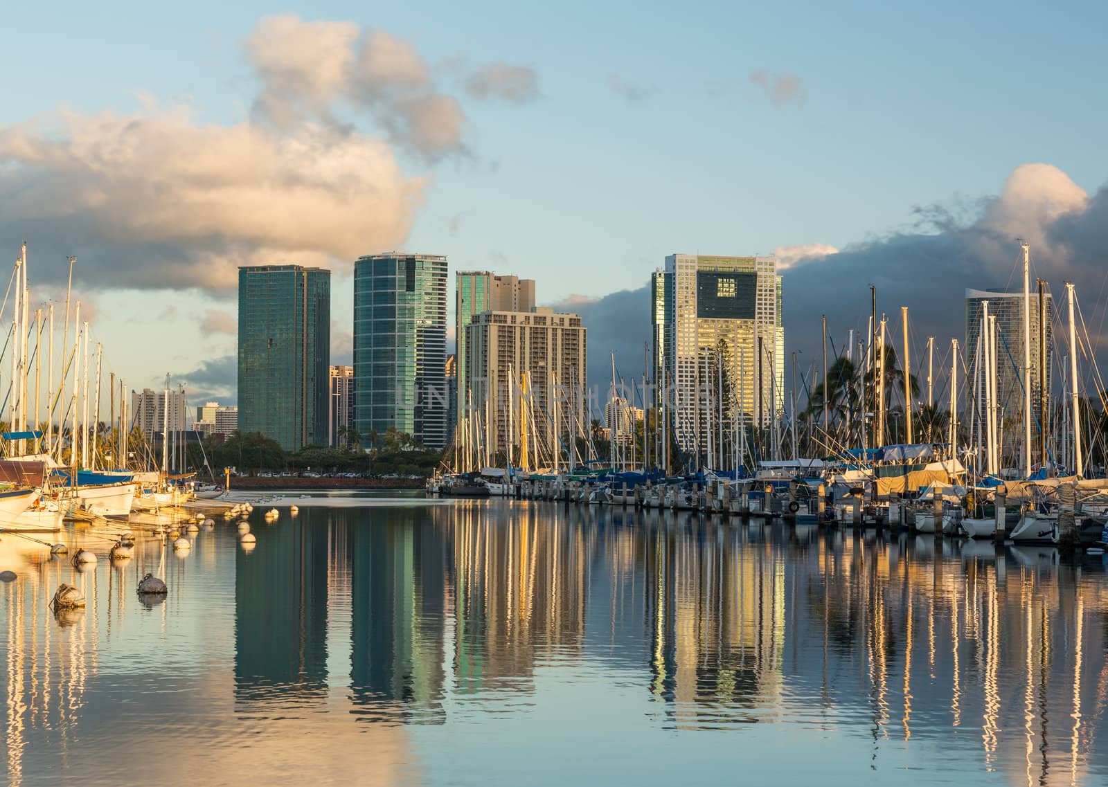Yachts line harbor at Ala Moana near Waikiki Oahu Hawaii with reflections of office and hotel buildings in still water