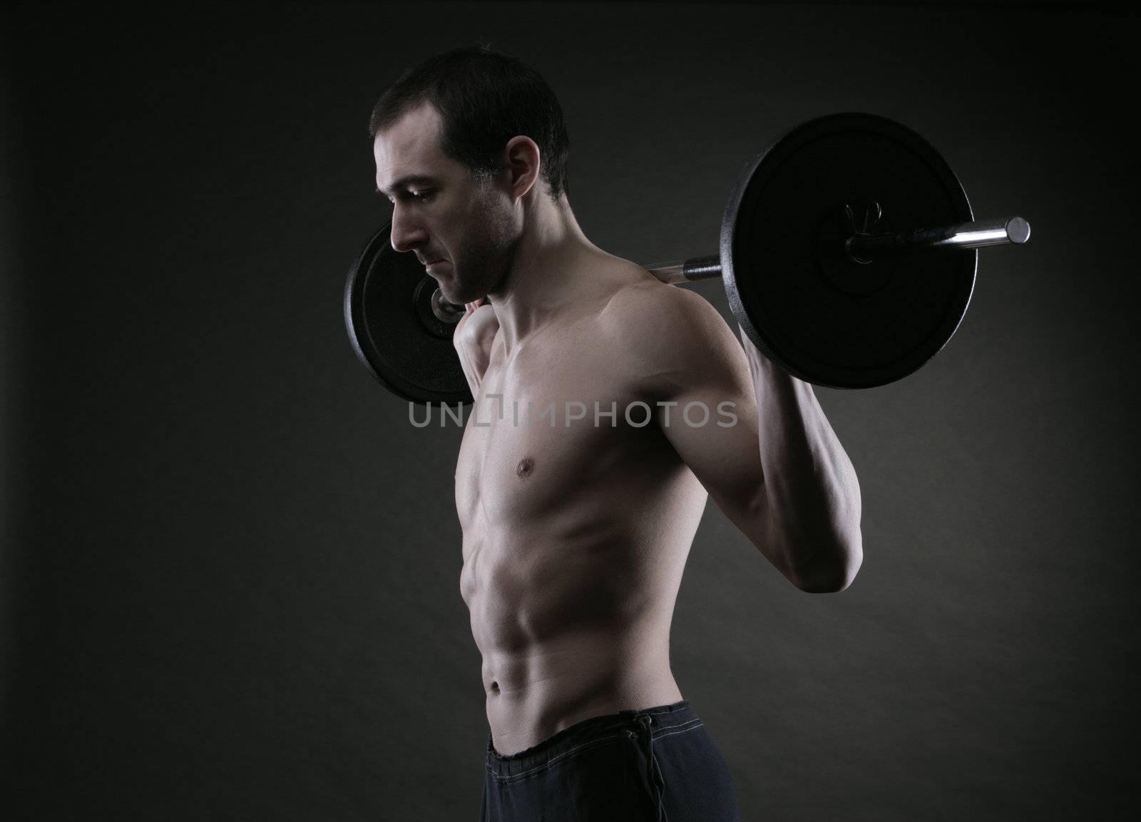 Muscular male athlete is training by lifting the barbell