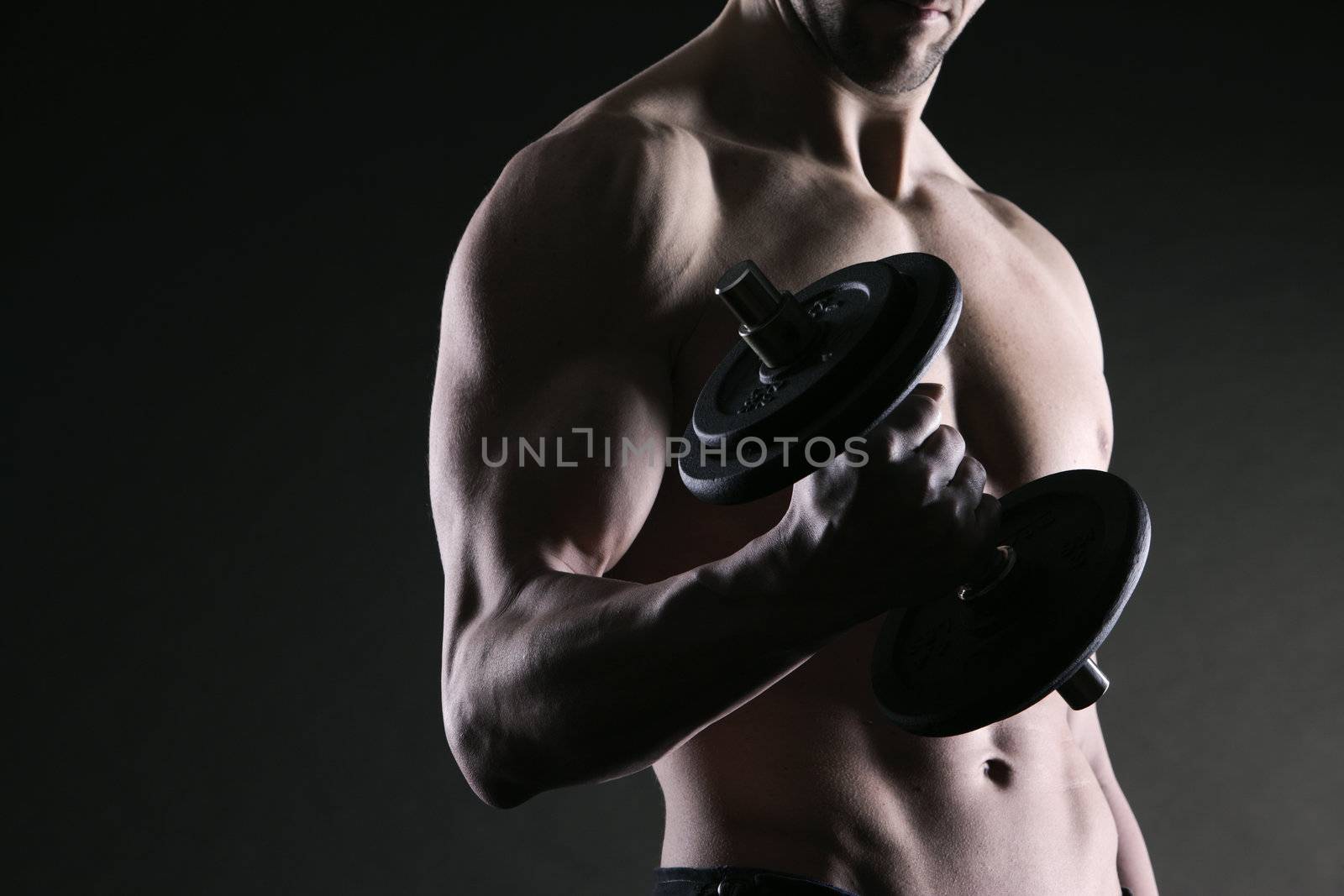 Muscular male athlete is training by lifting dumbbells