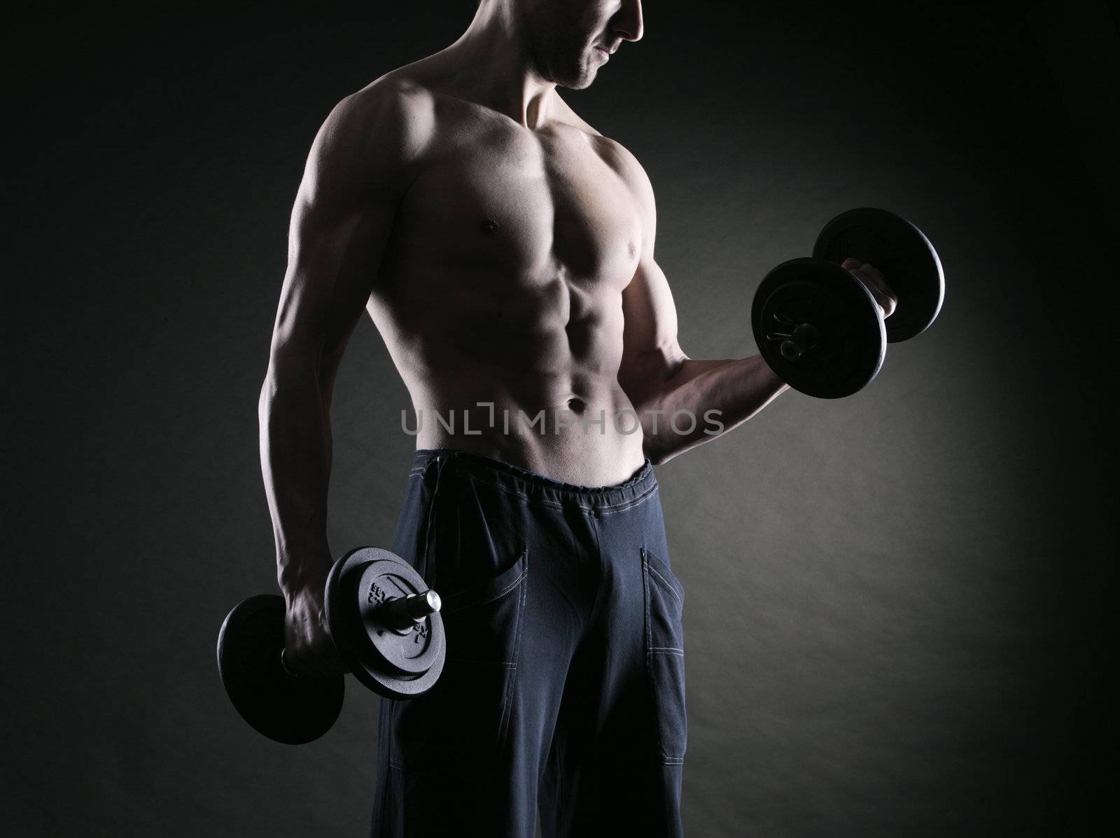Muscular male athlete is training by lifting dumbbells