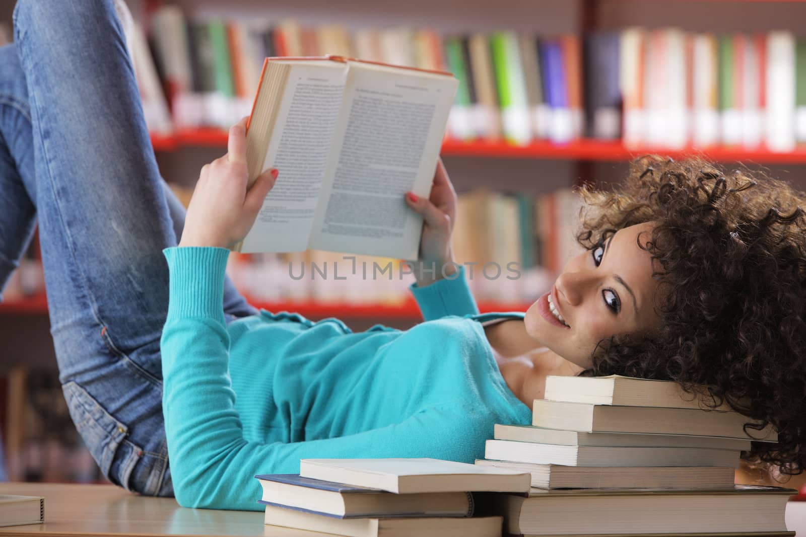 Portrait of beautiful female student in library reading a book