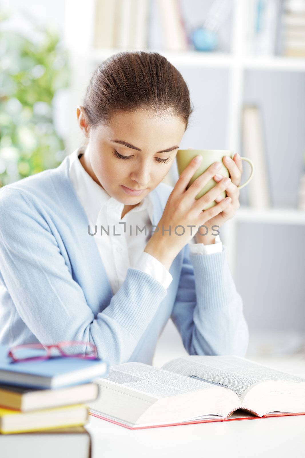 Beautiful female student reading a book with a cup of tea or coffee