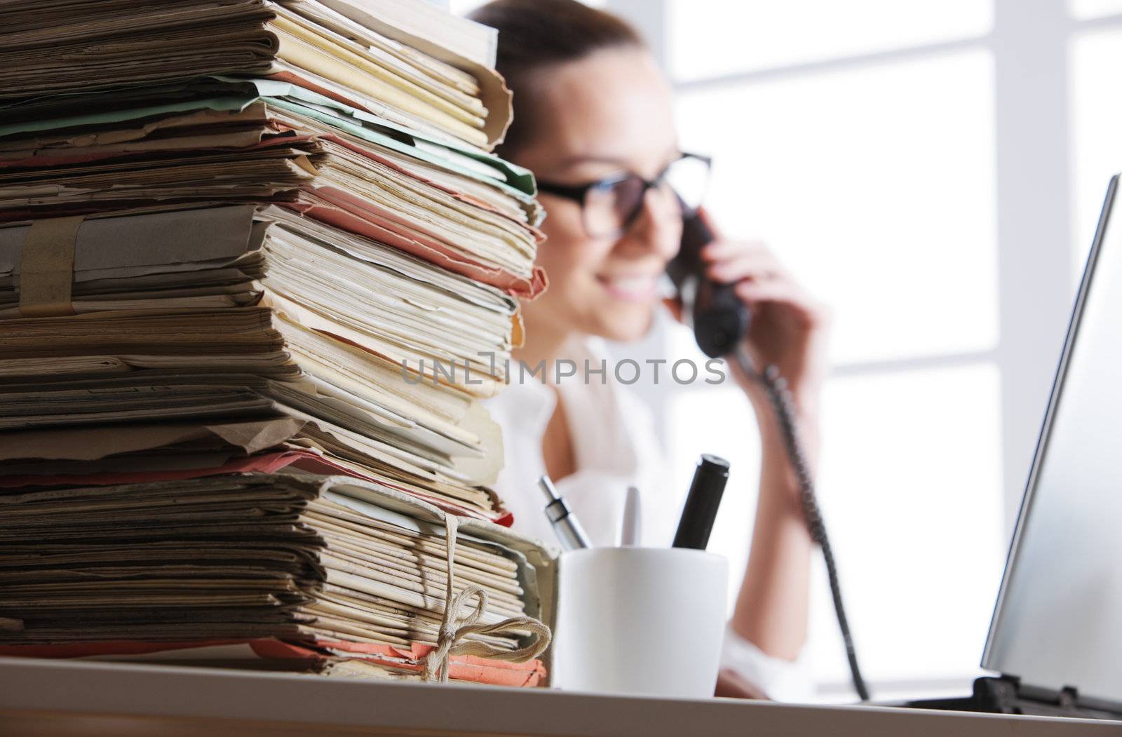 Stack of documents, secretary speaking on the phone in the background