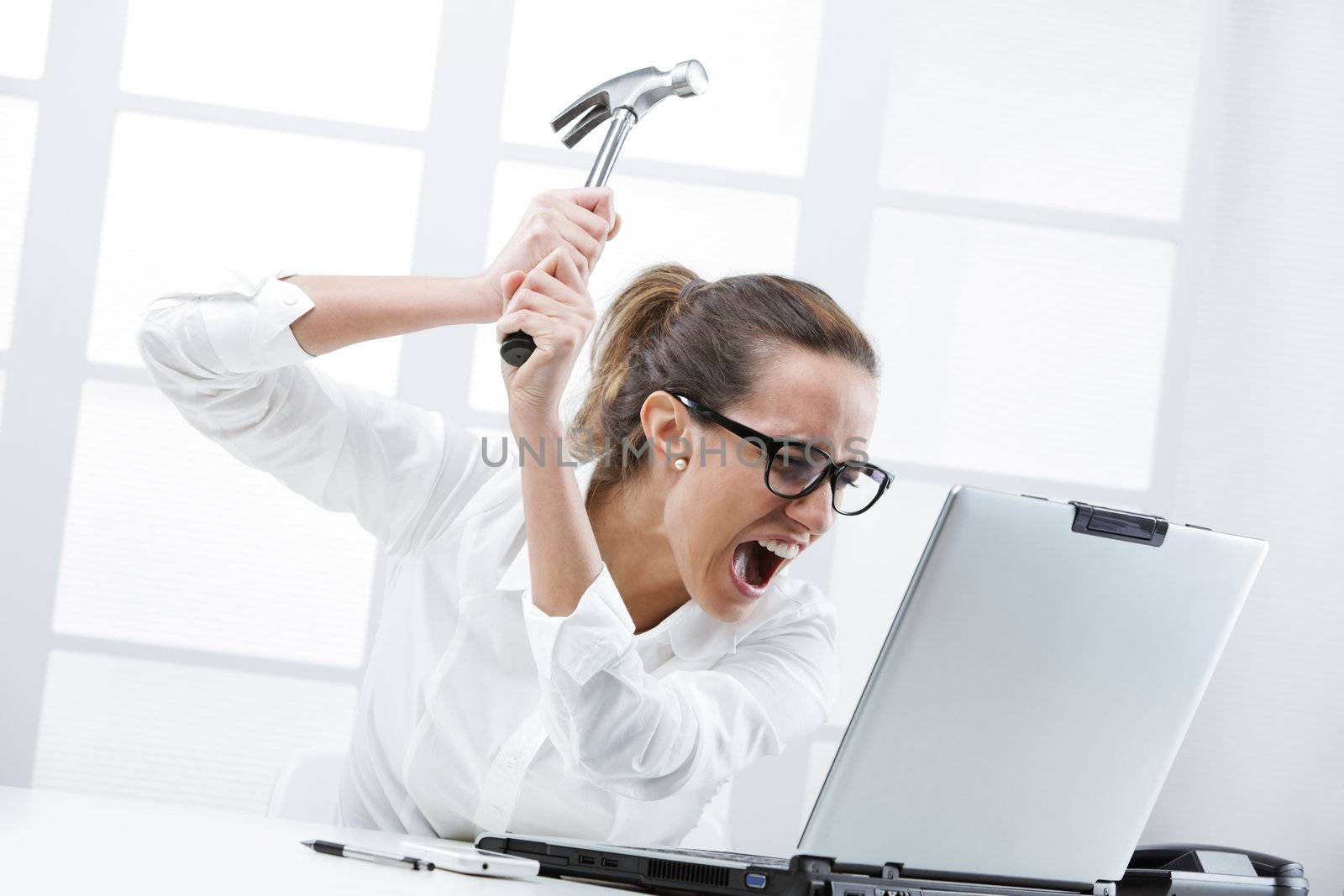 Freaked out business woman with a hammer ready to smash her laptop computer 