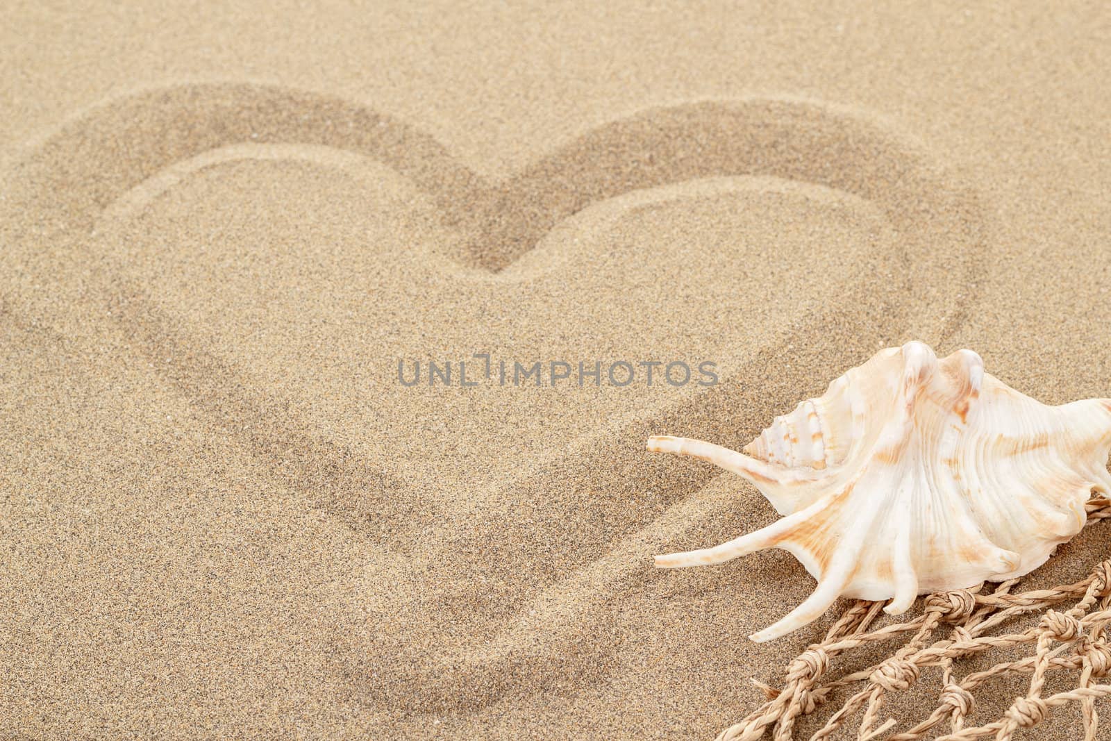 handwritten heart on yellow soft sand with seashell and shallow focus