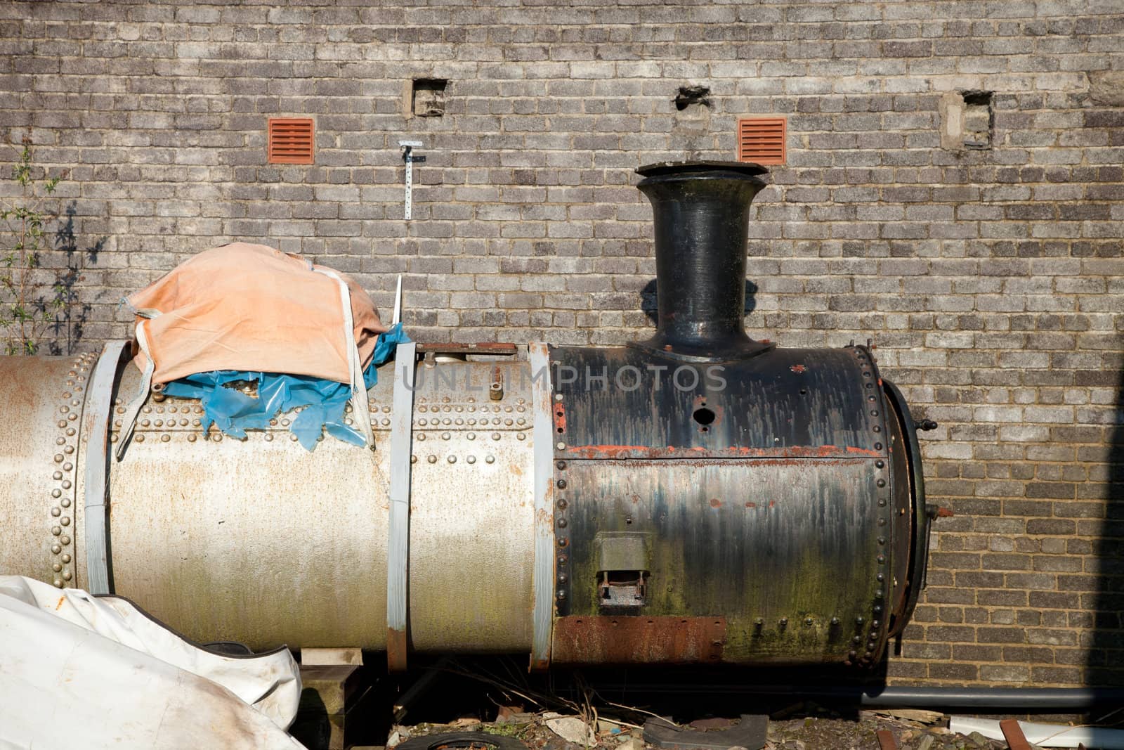 An antique, vintage, remains of a steam locomotive boiler section expossed from under tarpaulings.