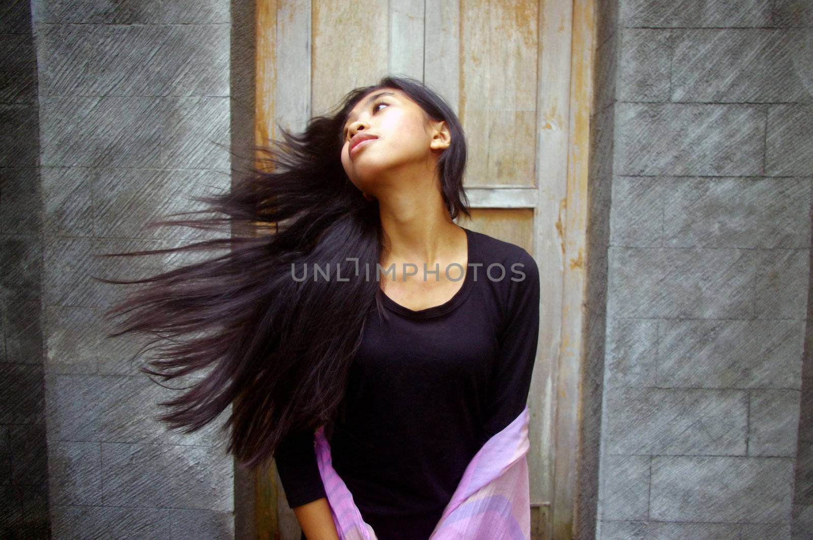 Young Asian woman flicking hair infront of wooden door.