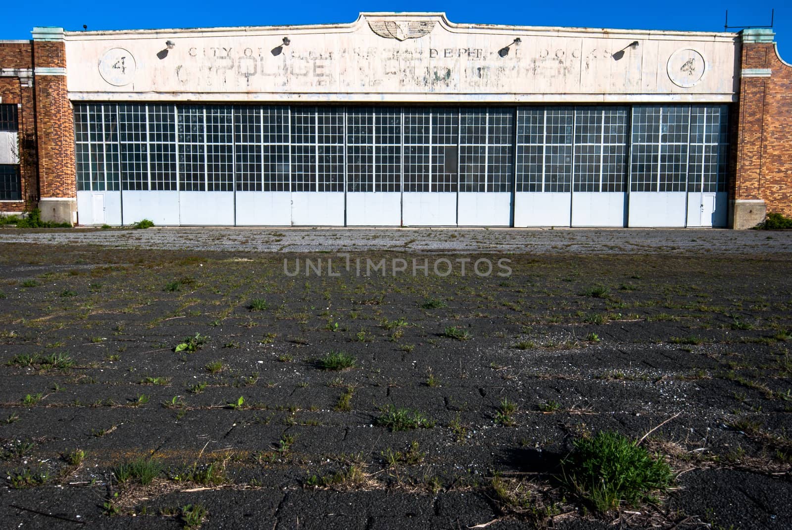 Photograph of an abandoned Aircraft Hangar with faded paint and text.  Weeds are growing up though the old tarmac.